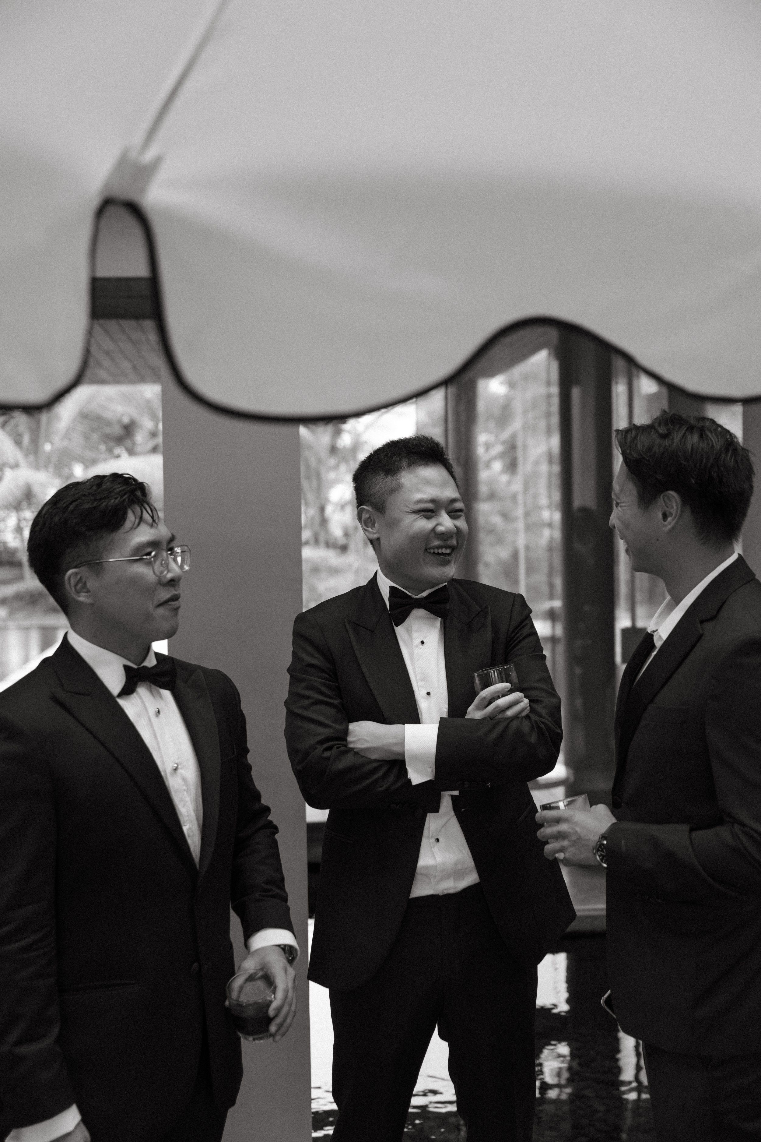 Guests in black tuxedos chatting during welcome drinks before Phuket destination wedding