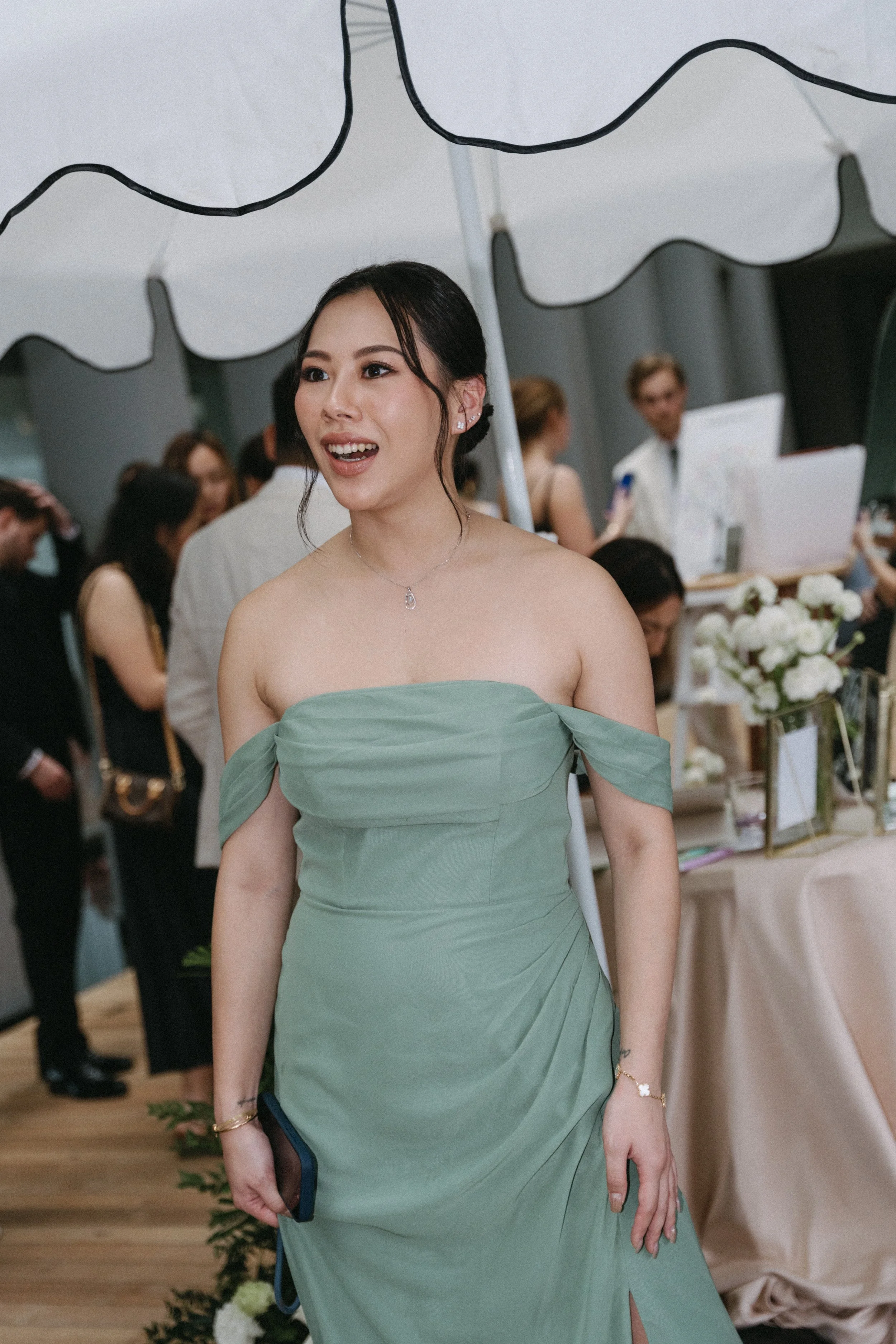 bridesmaid in off-shoulder sage green gown at pre-ceremony welcome drinks