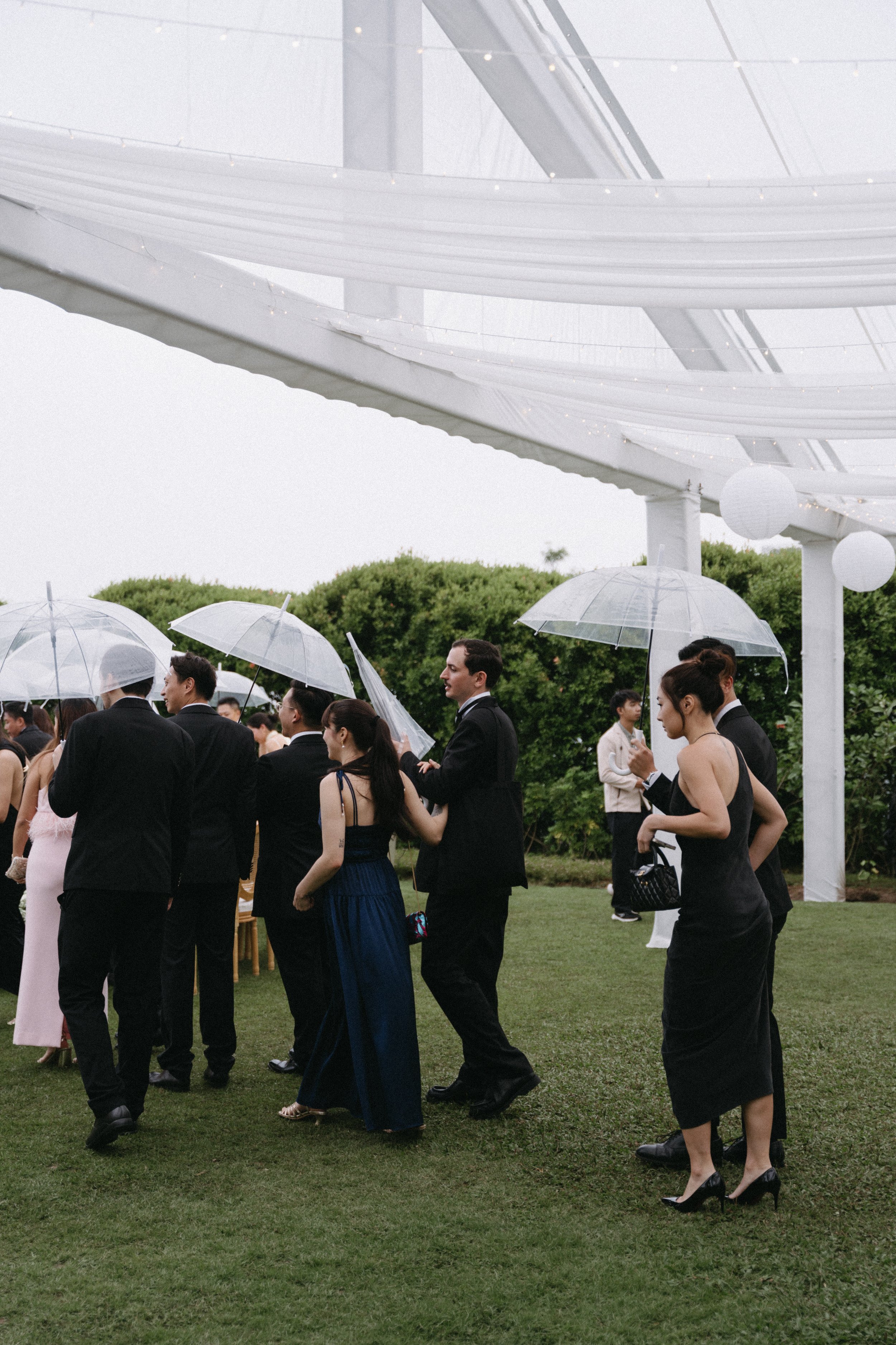 Wedding guests walking under umbrellas beneath draped white pergola at destination wedding