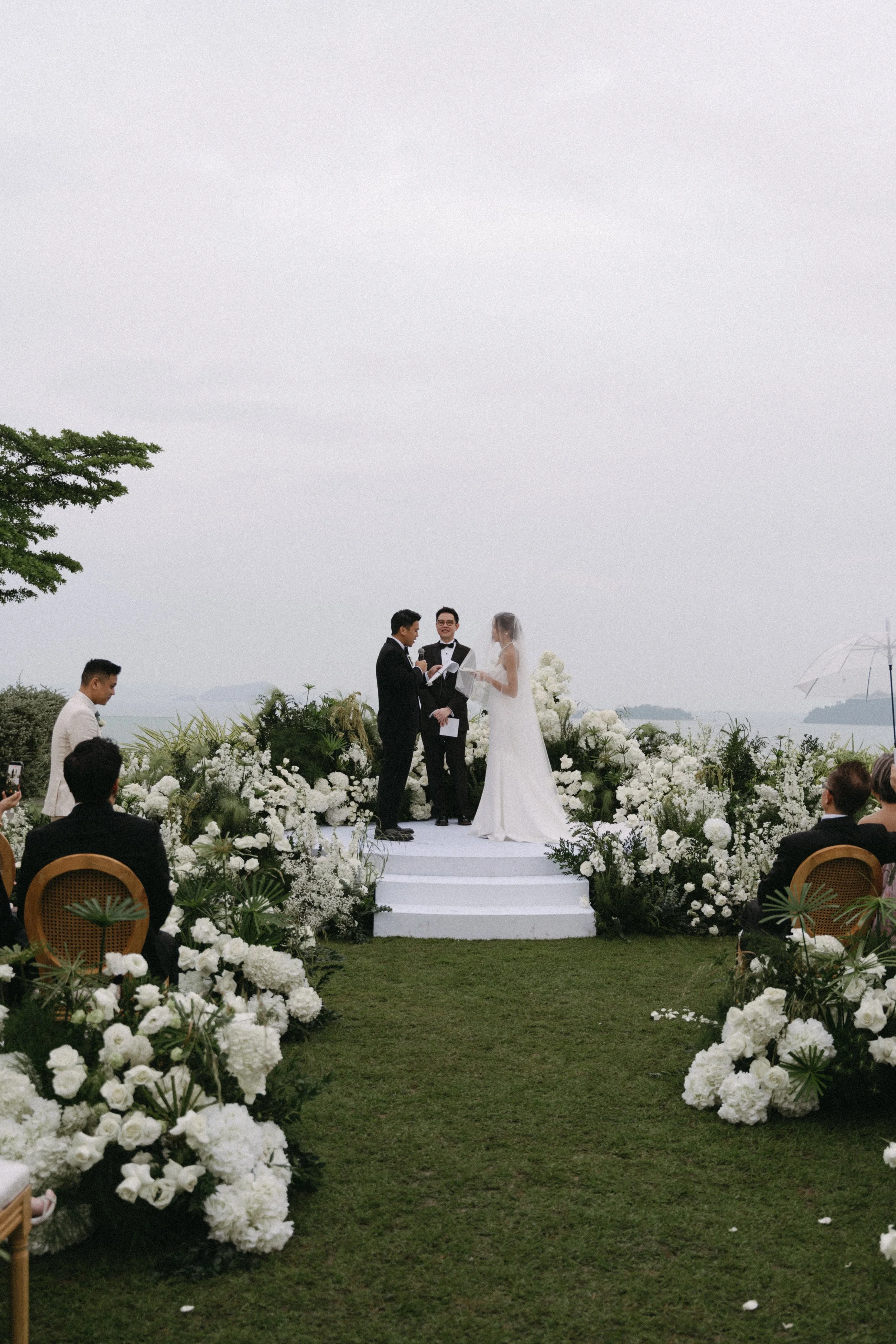 Wide shot of white floral-lined aisle leading to circular ceremony platform overlooking the ocean