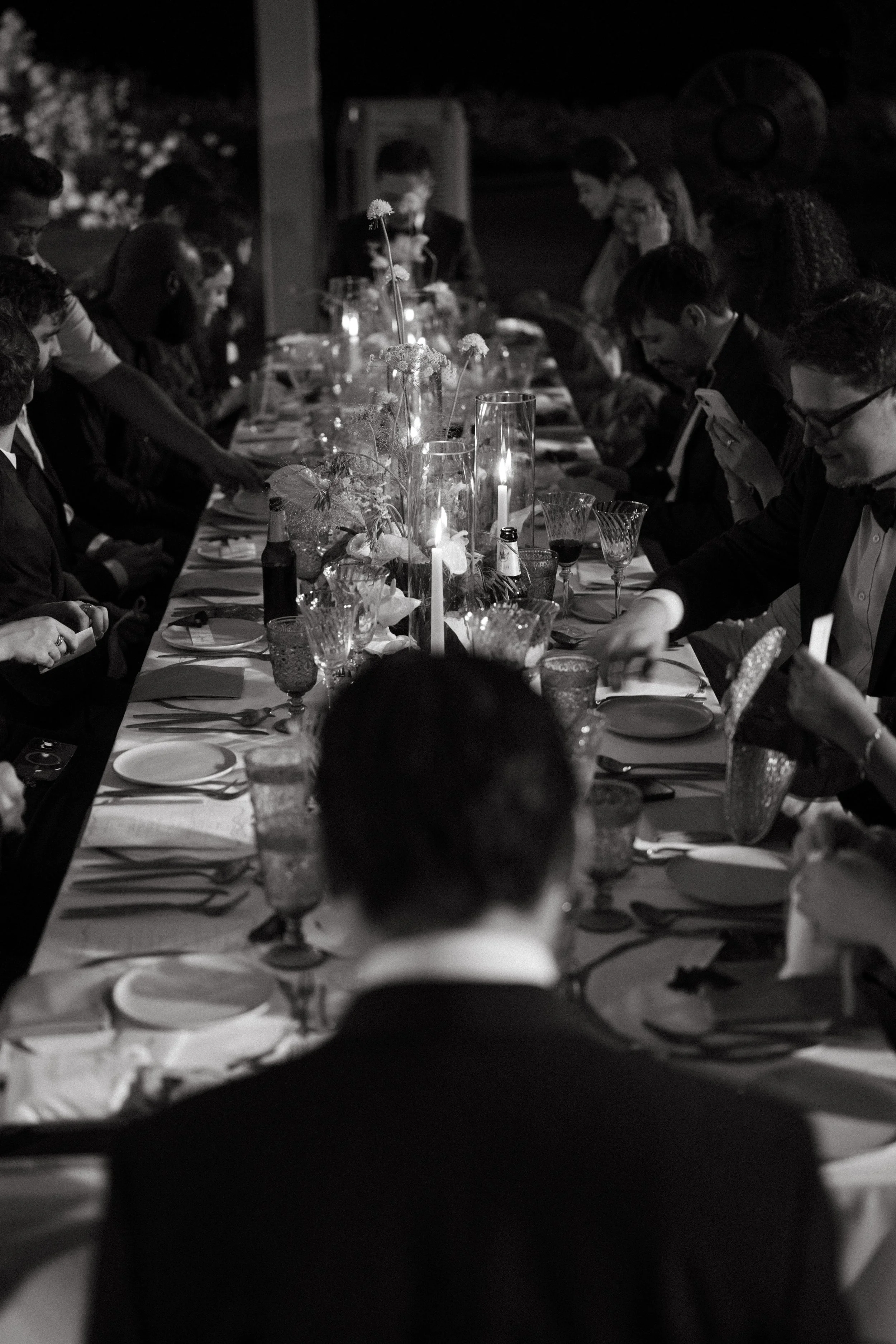 Long candlelit reception table viewed from behind guests, evening wedding dinner