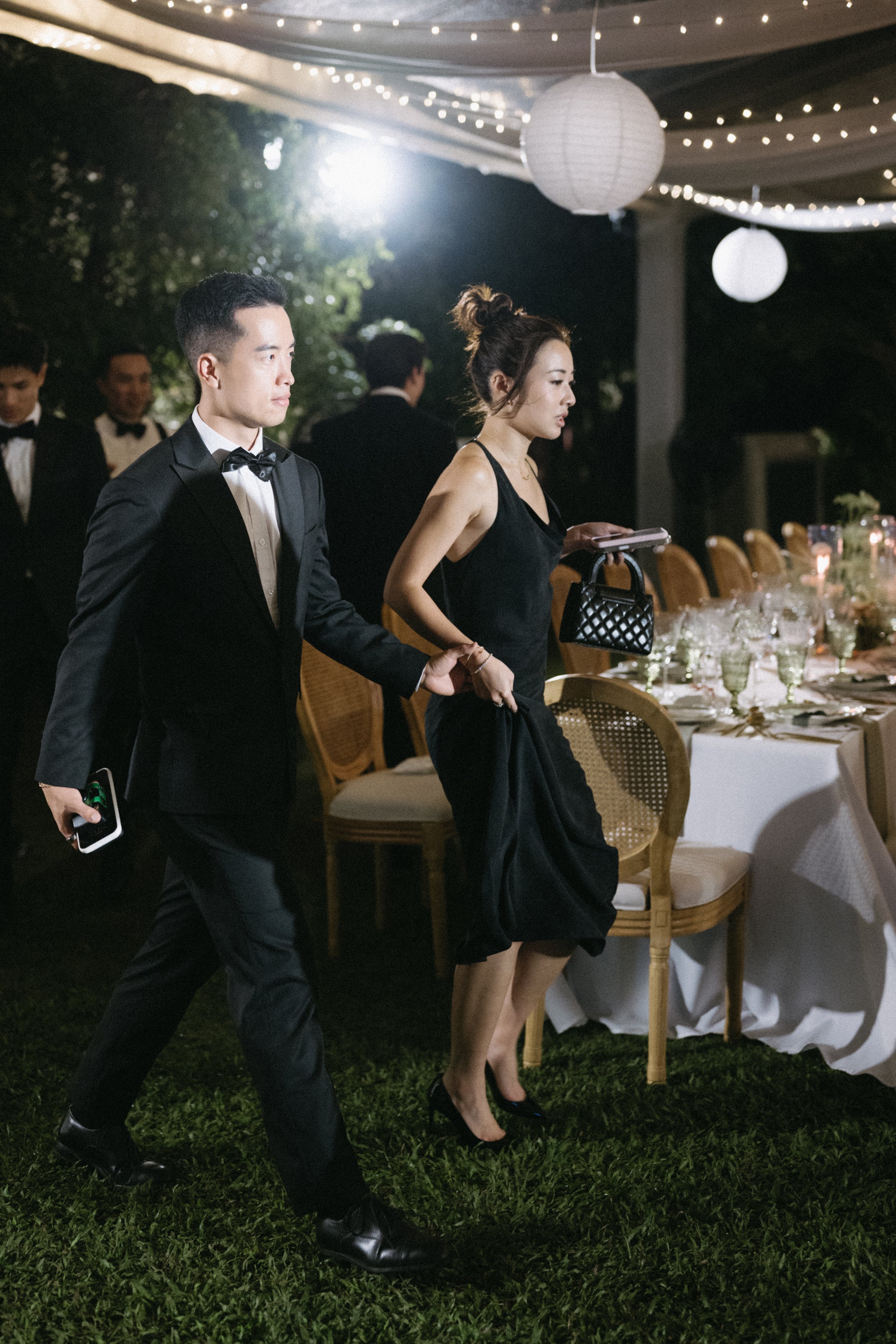 Guests walking past reception tables lit with paper lanterns at night