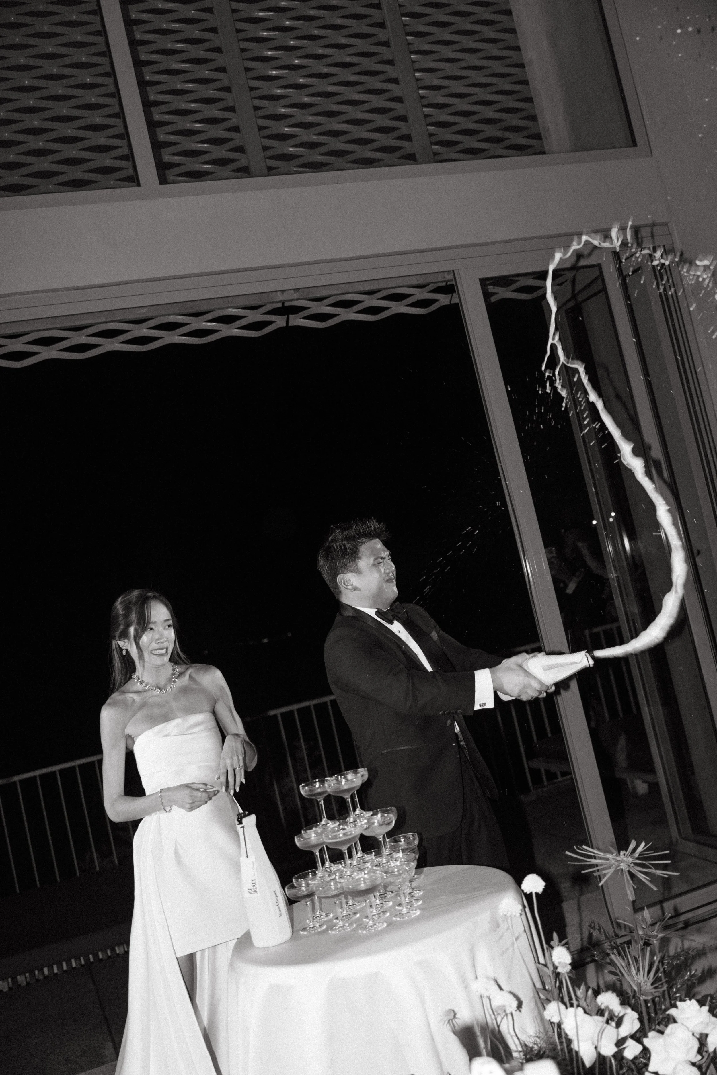 groom popping and spraying champagne bottle next to bride at reception