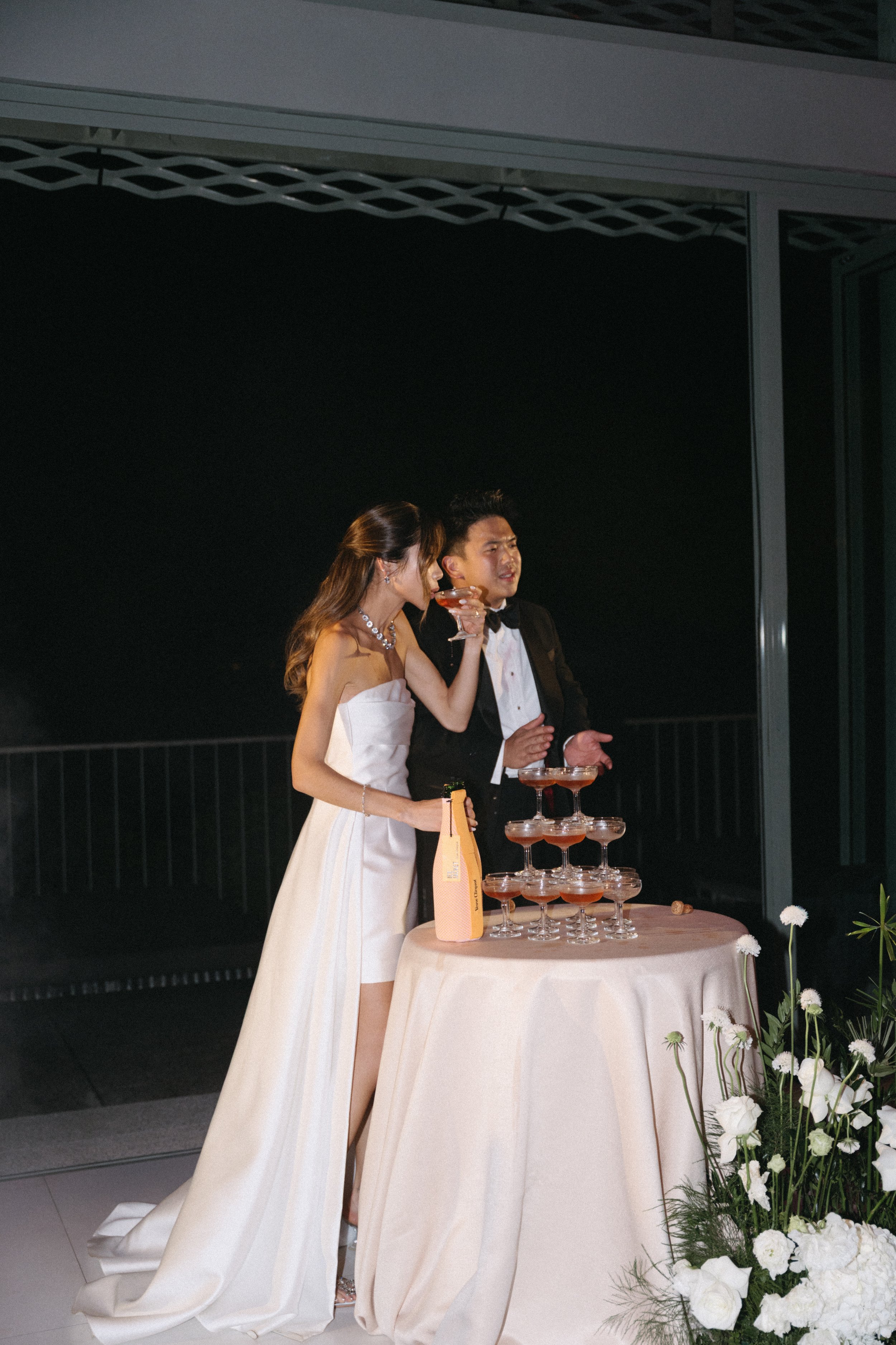 Newlyweds standing next to champagne tower at night reception