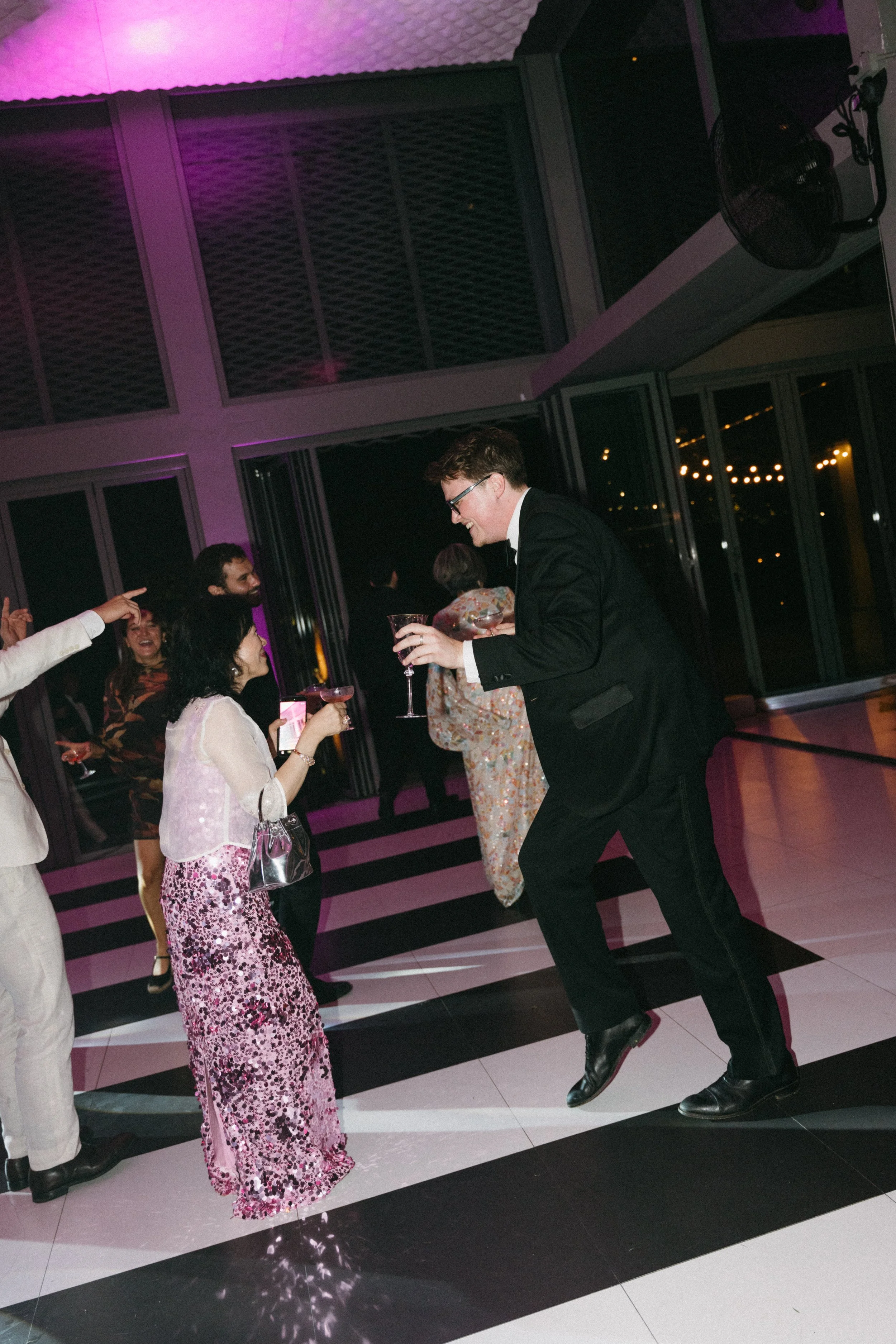 Guests dancing under blue and pink party lights on reception dance floor