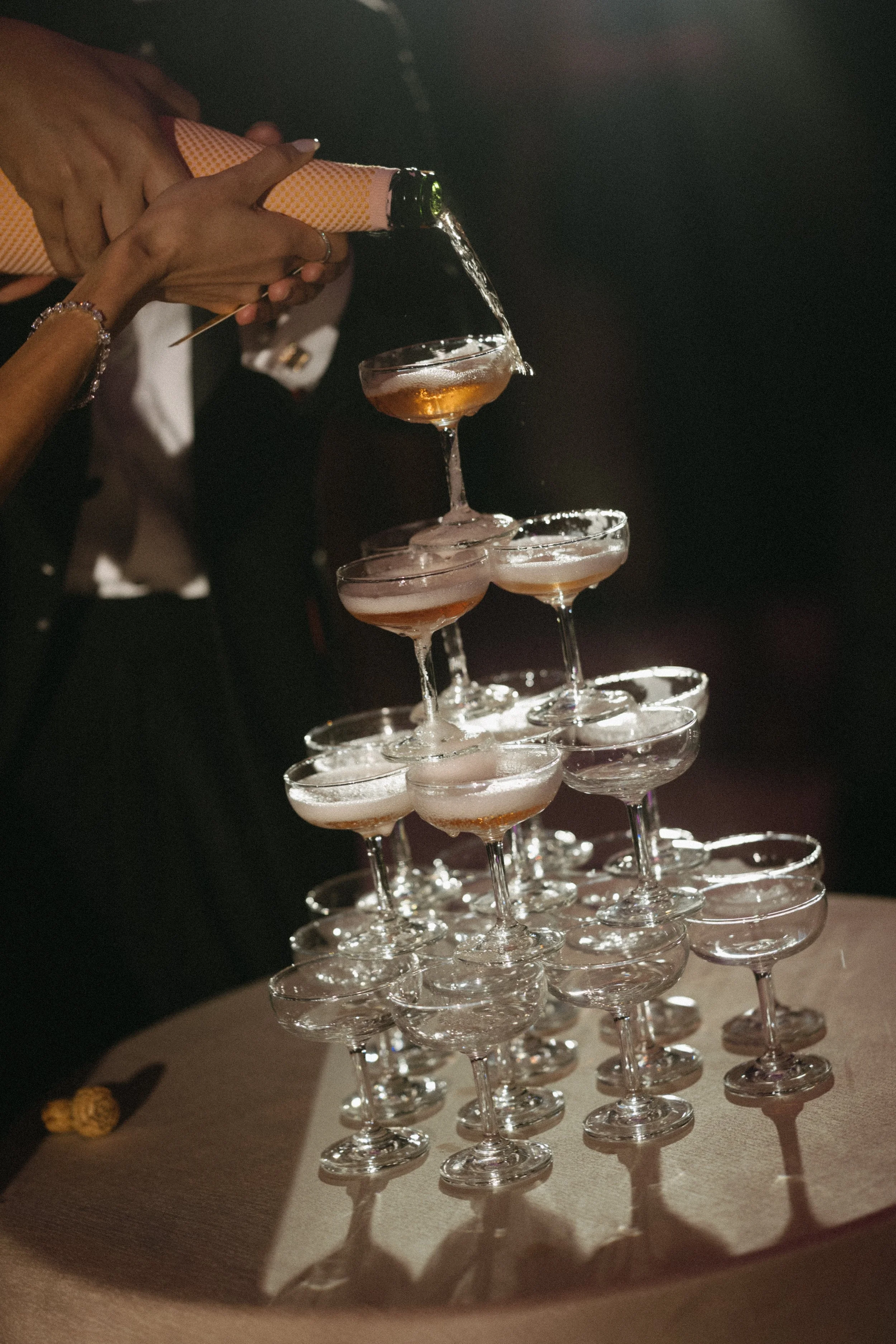 Champagne tower being poured at night reception, glasses catching the light