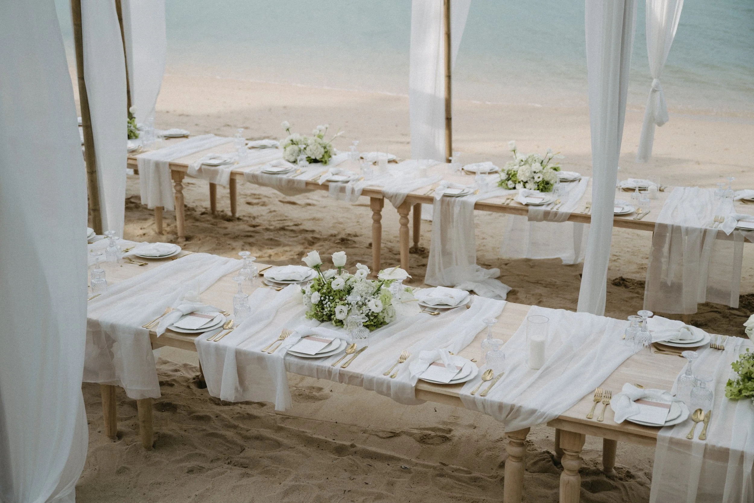Luxury outdoor beach wedding reception at Odyssey Mansion Koh Samui featuring long banquet table with white linen runner, floral centrepieces and ocean views on Bangrak Beach
