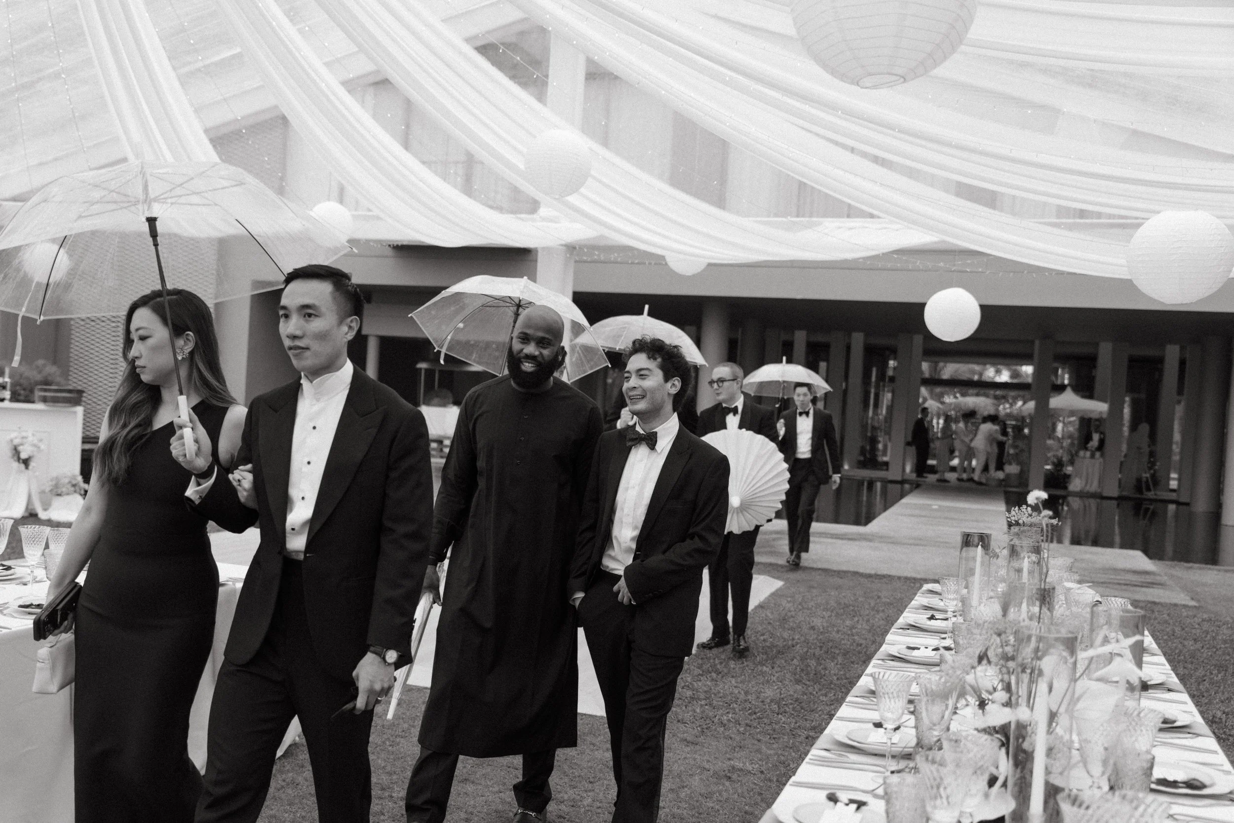 editorial black and white portrait of guests holding umbrellas while walking to ceremony