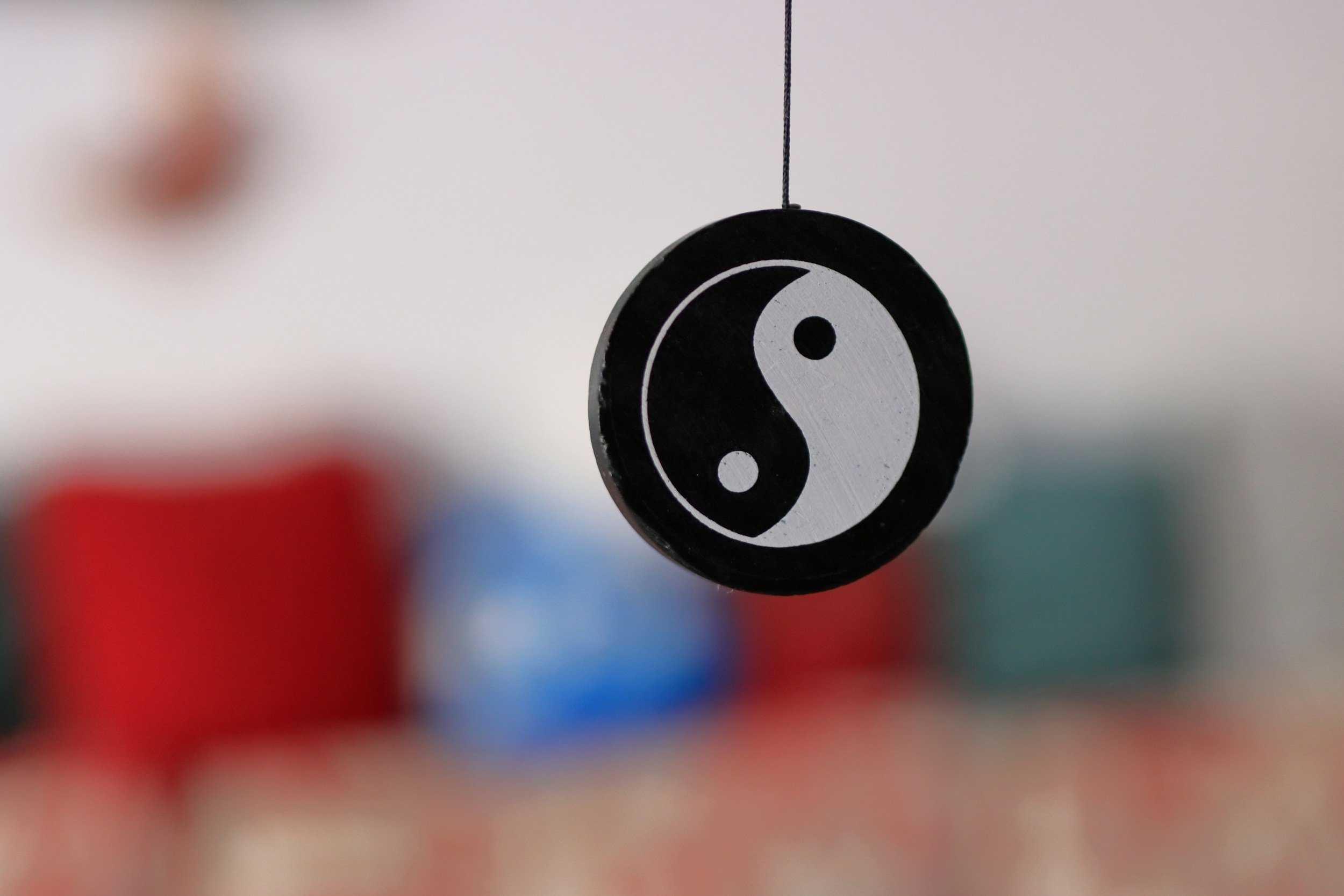 Yin yang symbol hanging against a blurred background with colorful cushions.