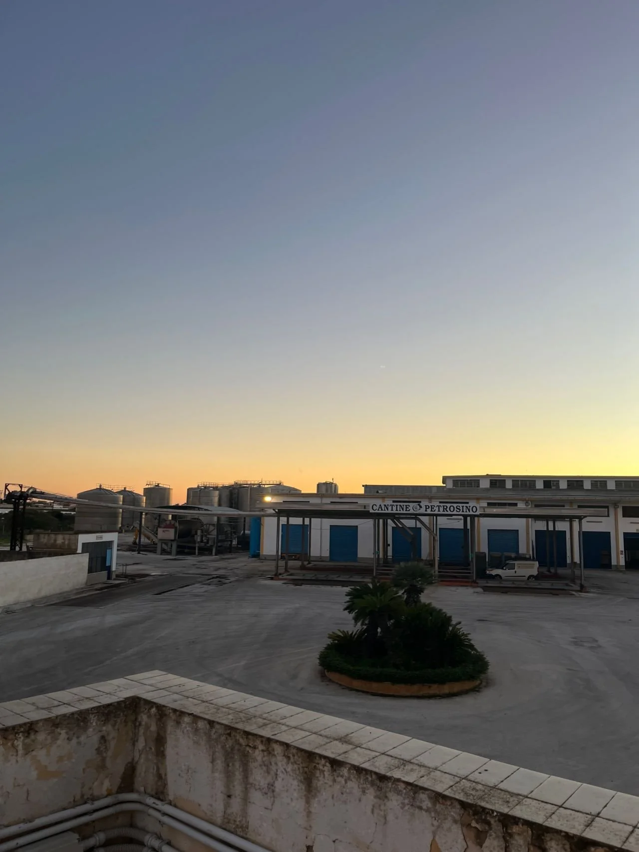 View of an industrial area during sunset with multiple storage tanks and a building labeled 'CANTINE PETROSINO.'