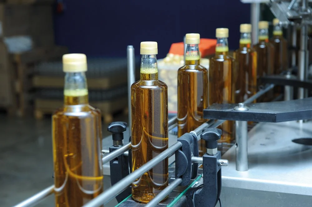 Bottles with amber liquid on a conveyor belt in a production facility.