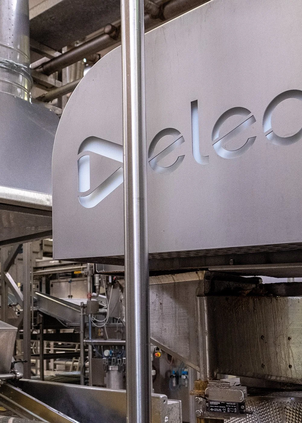 Industrial machinery with stainless steel components and a logo part visible, indicating "ele" from a brand name, in a manufacturing setting.