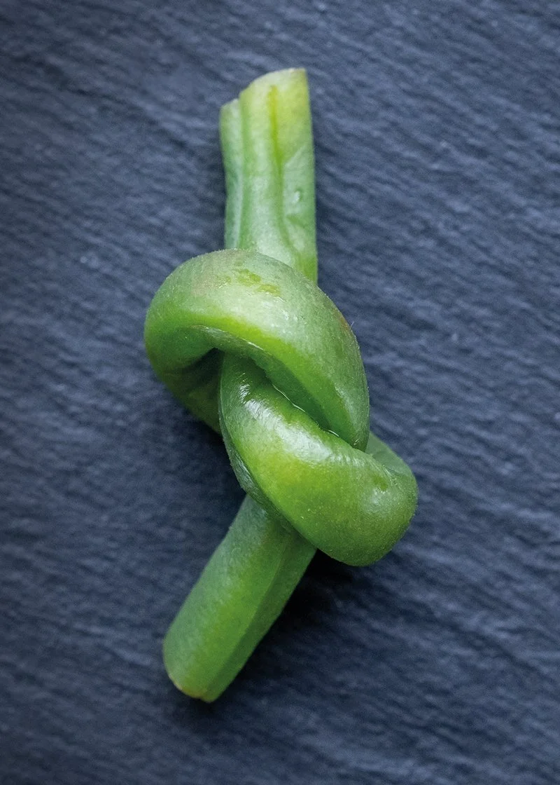Green bean tied in a knot on a dark surface