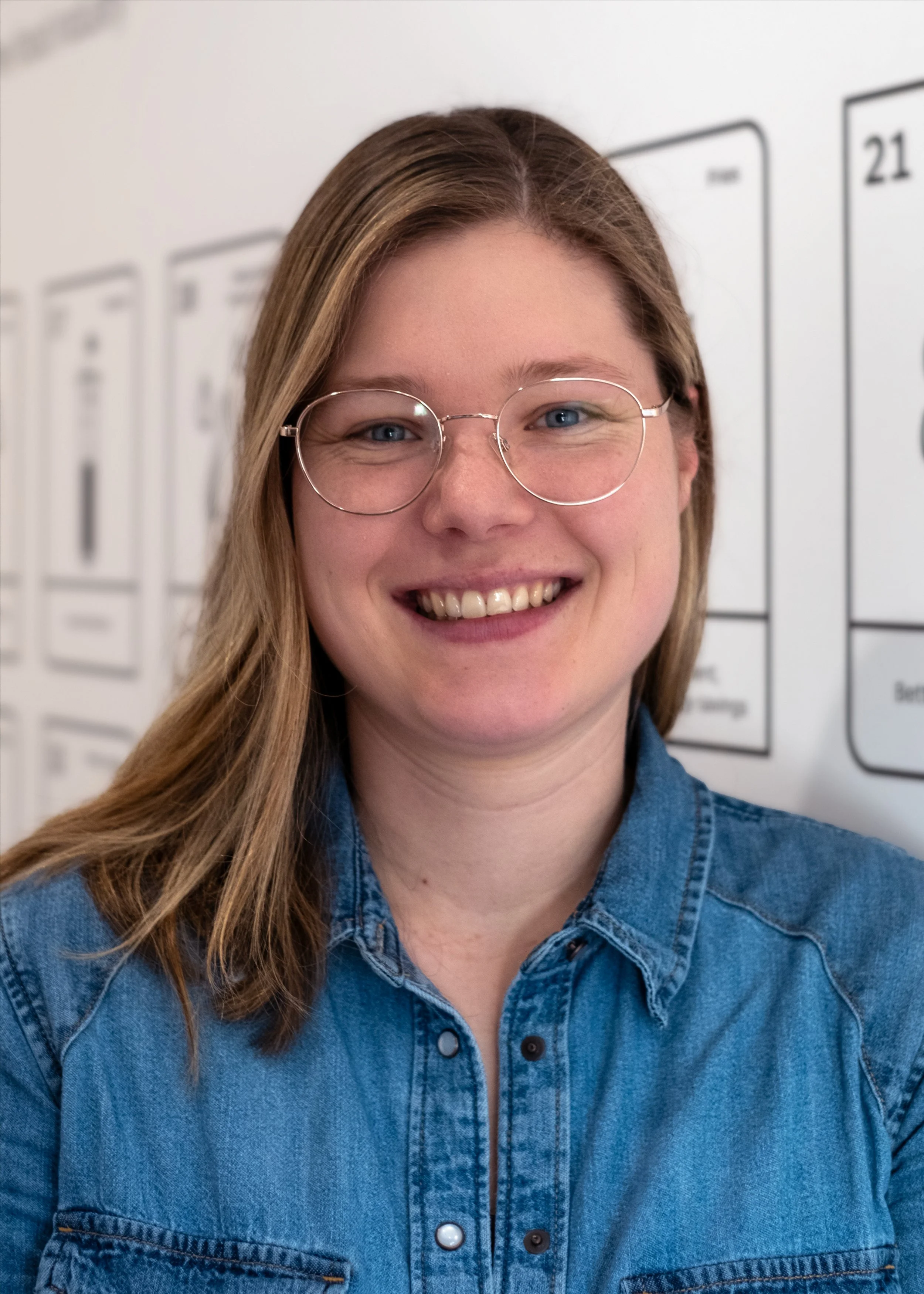 Smiling person wearing glasses and a patterned blouse in an indoor setting.