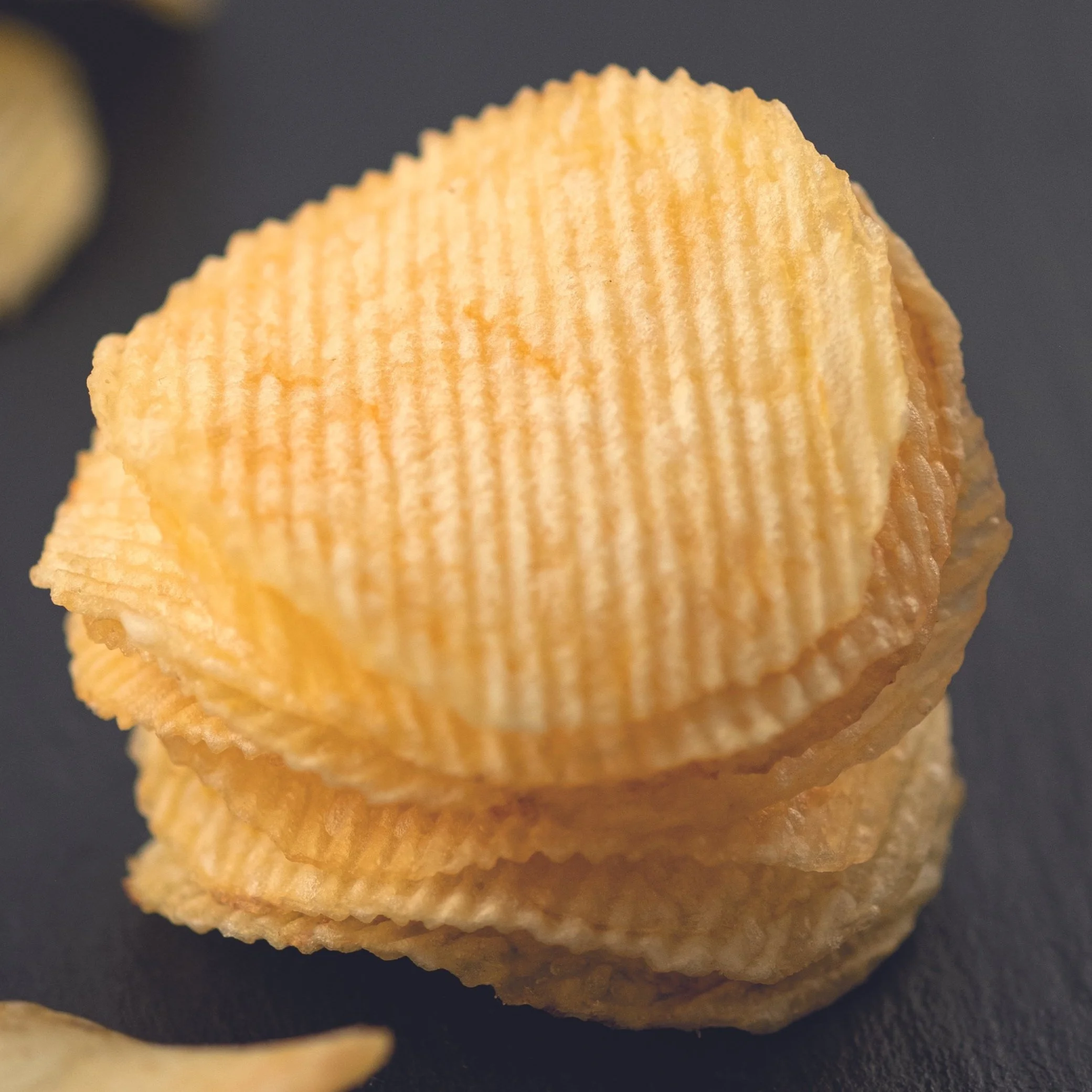 Close-up of stacked ridged potato chips on a dark surface.