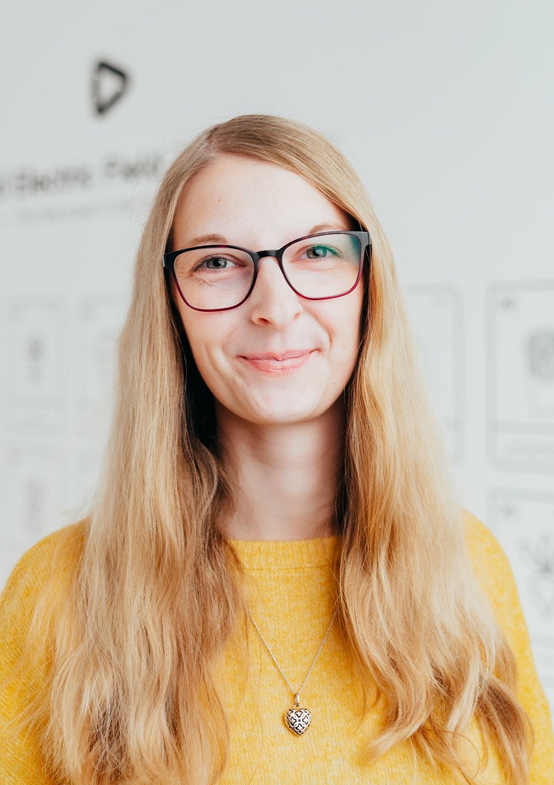 Woman with long blonde hair wearing glasses, a yellow sweater, and a heart-shaped necklace.