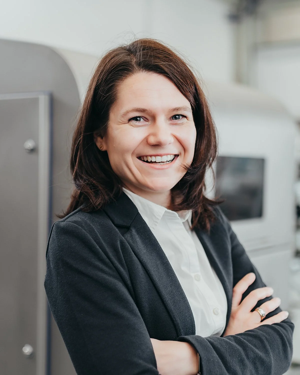 Smiling woman in business attire standing with arms crossed indoors.