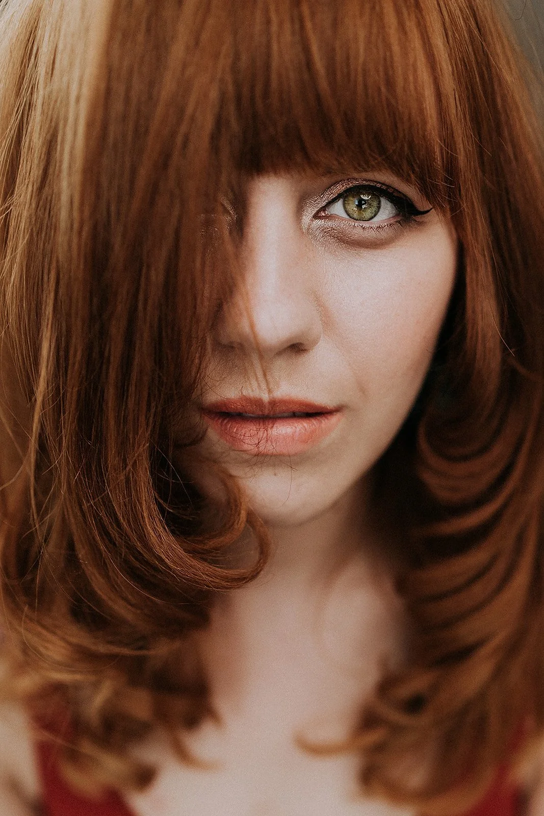 Close-up of a person with long auburn hair and green eyes, partially covered by hair.