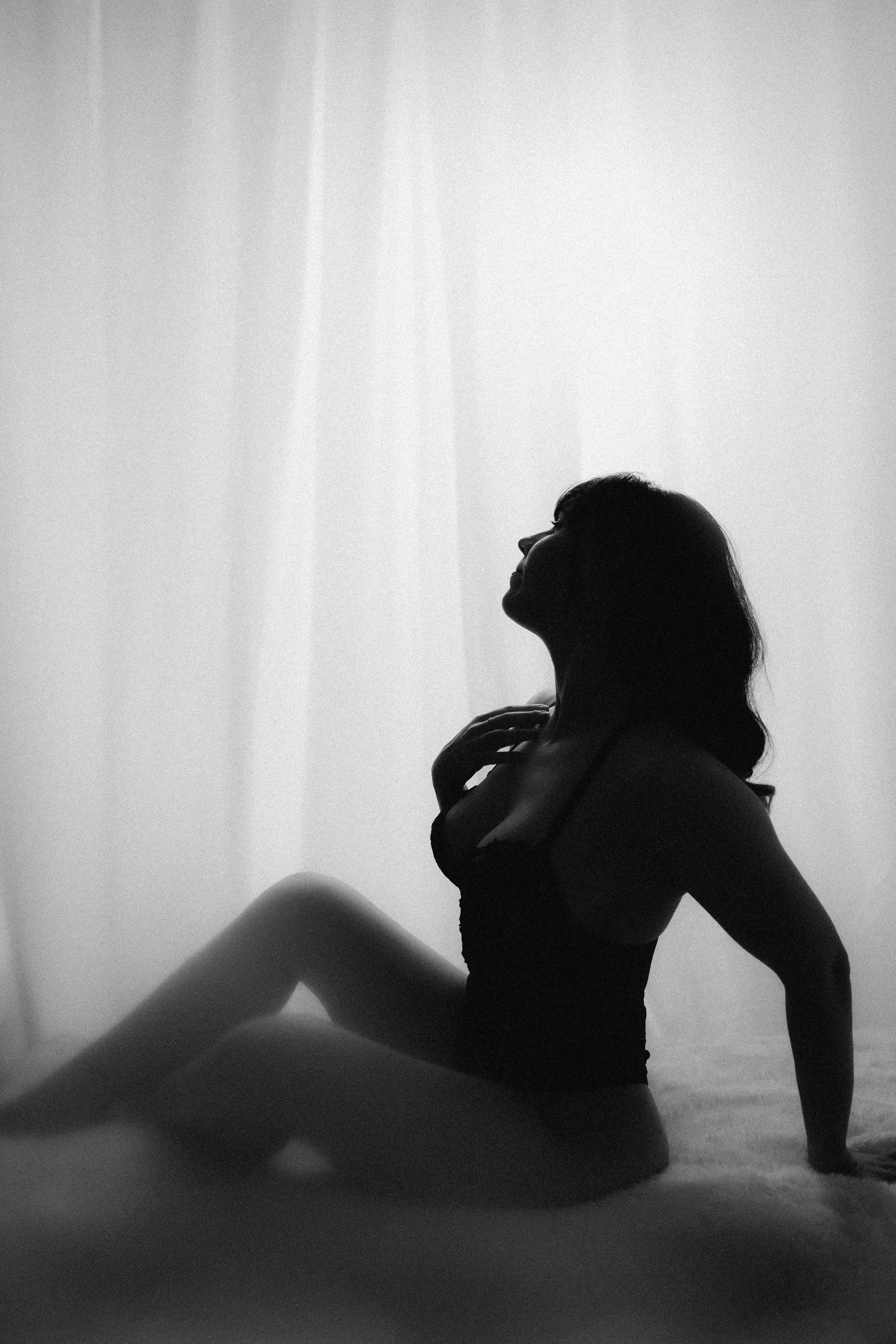 Silhouette of a woman in lingerie sitting on the floor with soft lighting.