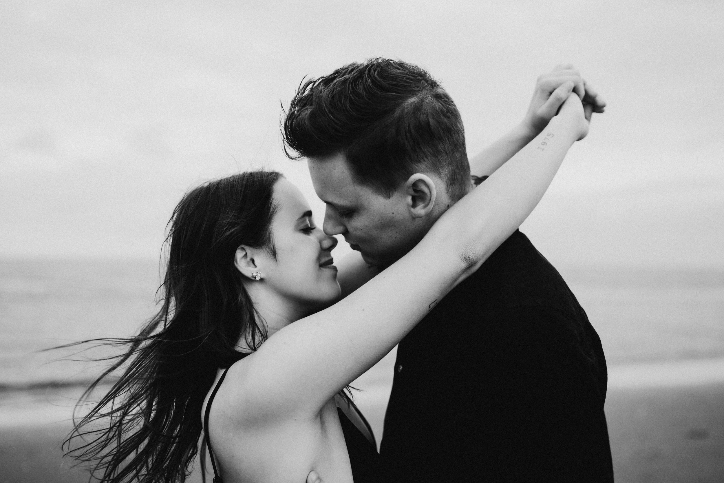 A couple embracing closely on a beach, with eyes closed, in black and white