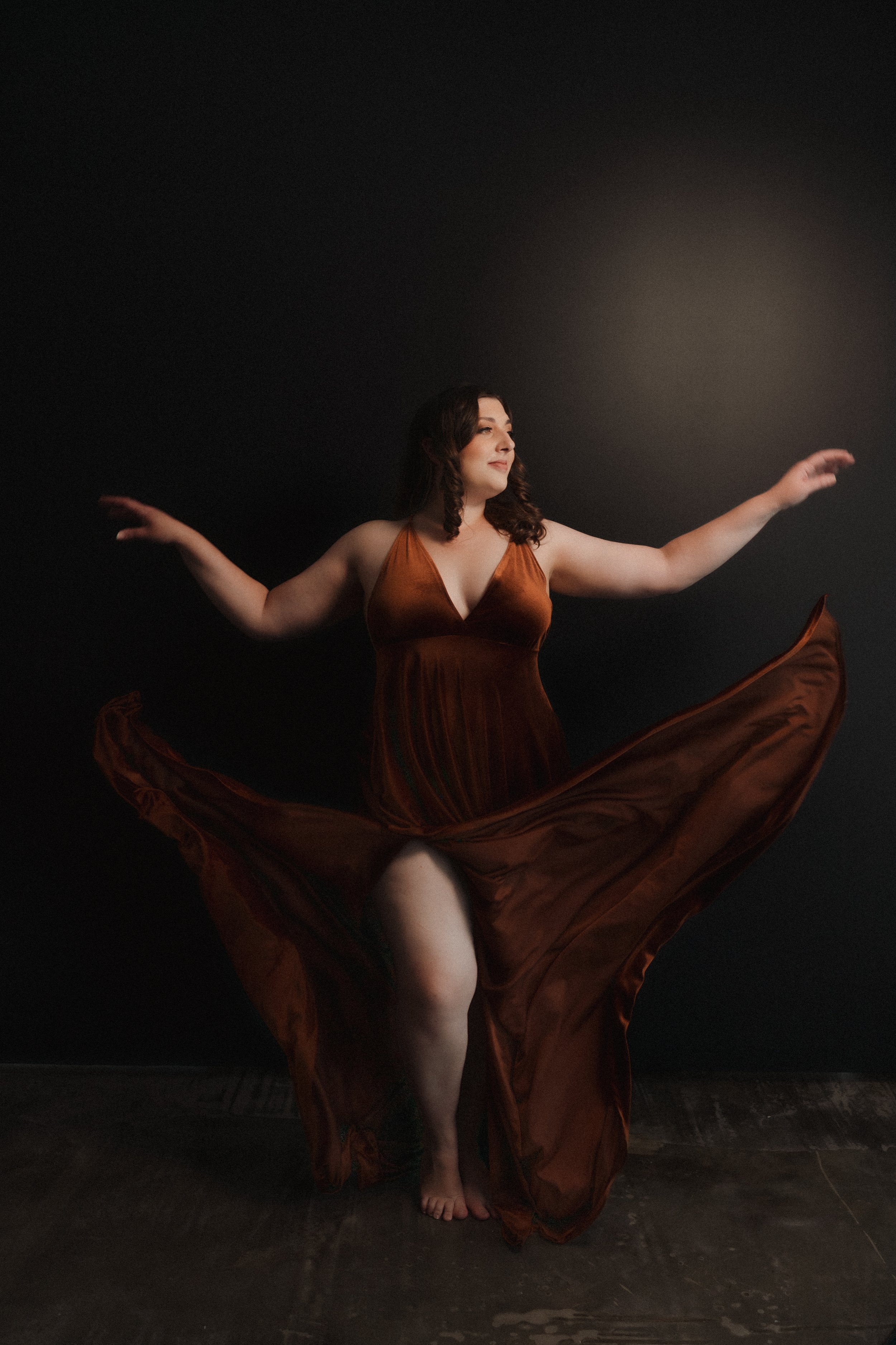 Woman in a flowing brown dress dancing gracefully against a dark background.