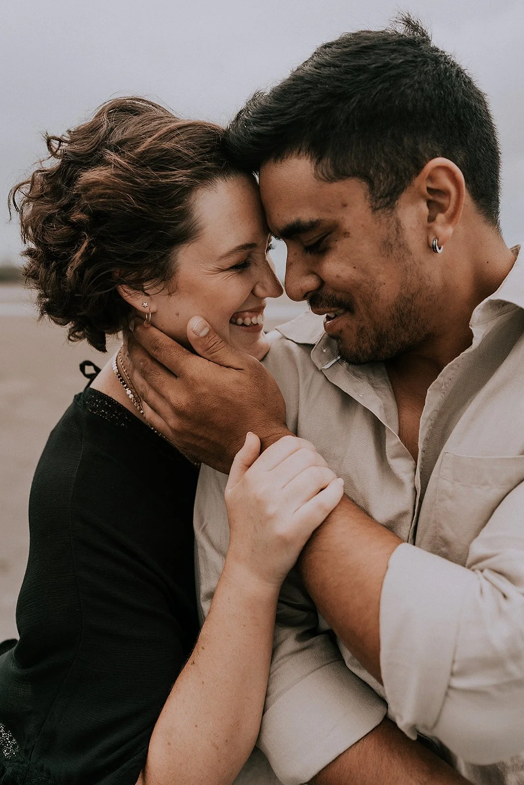 A couple sharing an intimate moment with their foreheads touching, eyes closed, smiling, outdoors.