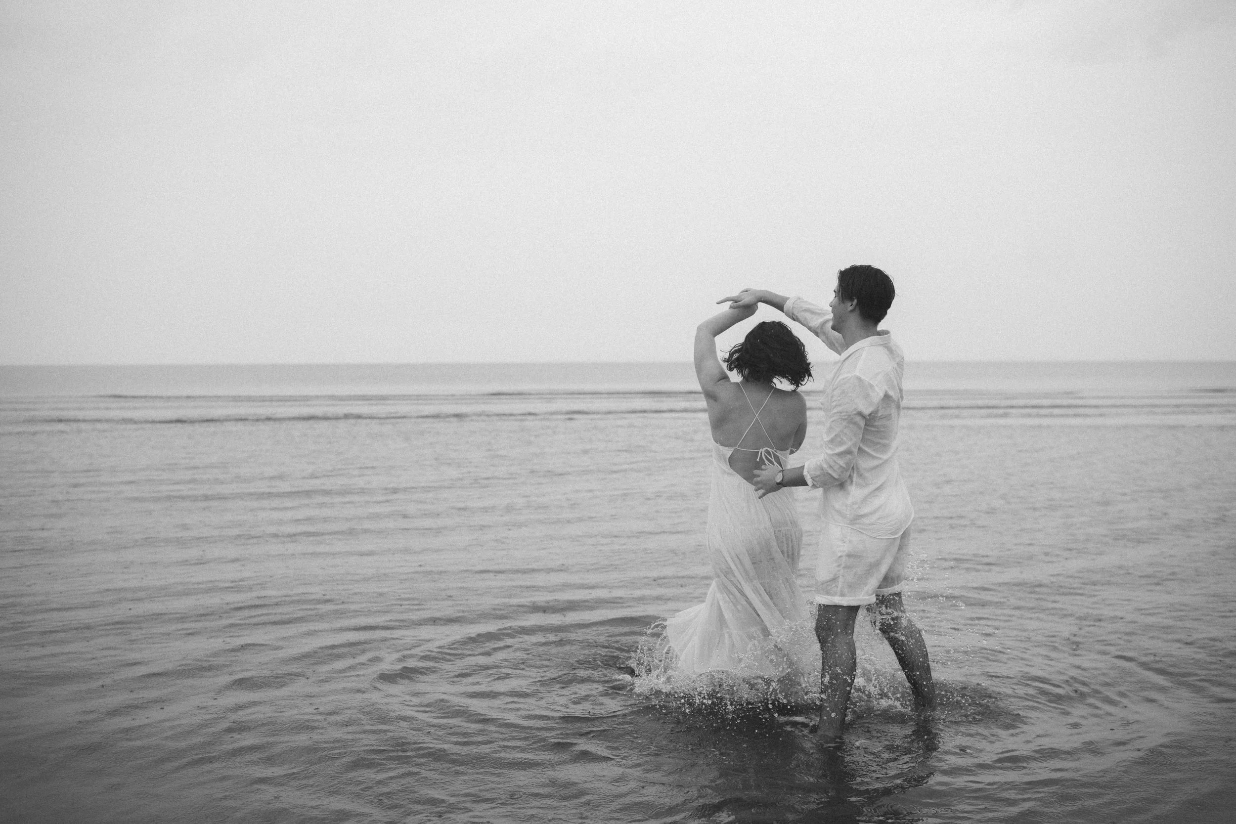 A black and white photo of a couple dancing in the ocean's shallow water.