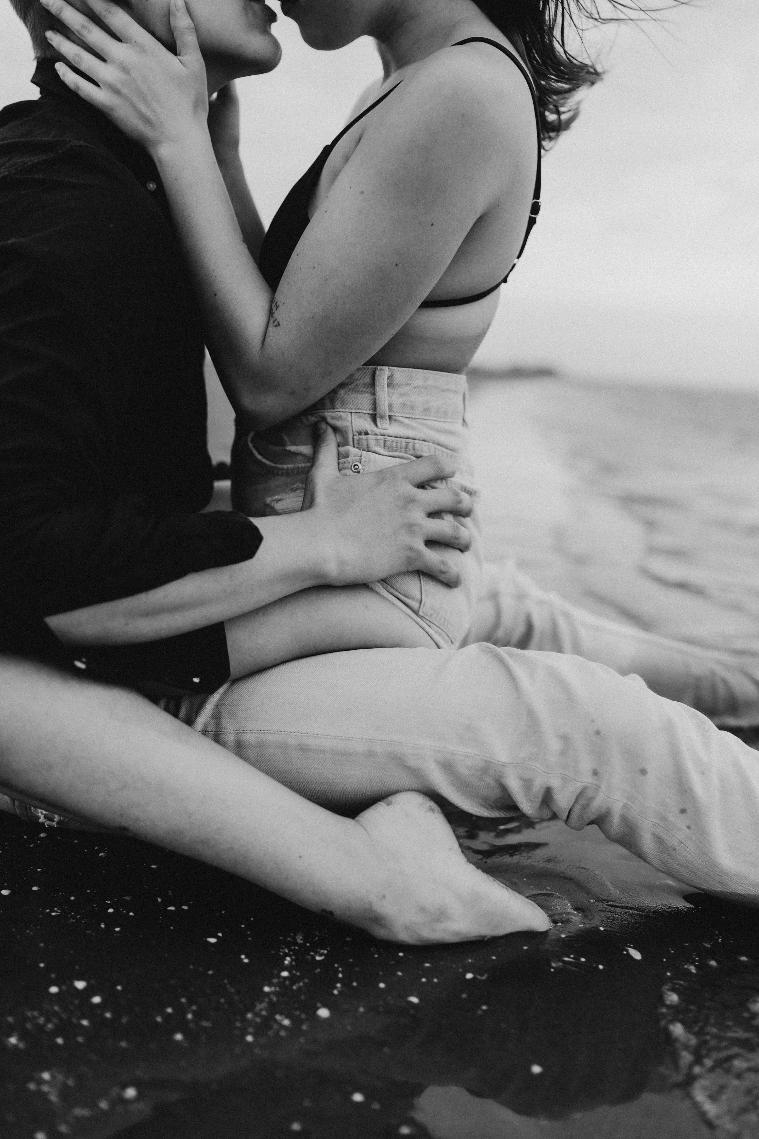 Couple sitting on the beach, embracing and kissing, in black and white.