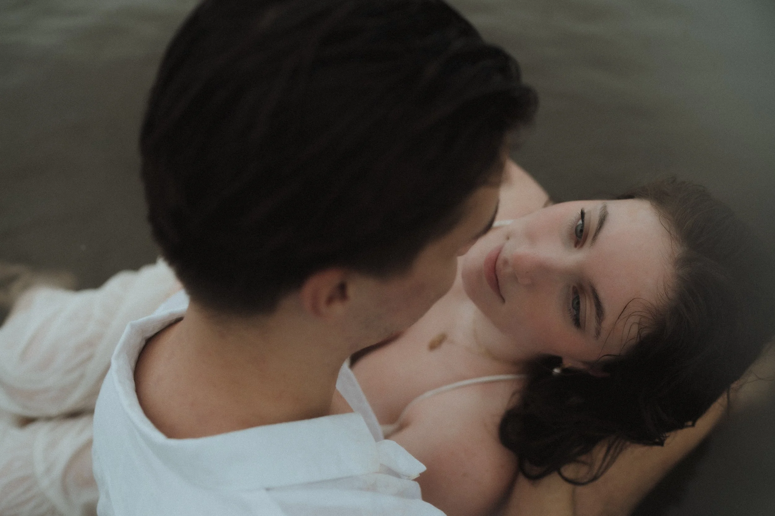 A man and a woman lying close together on the ground, gazing into each other's eyes during a romantic moment.