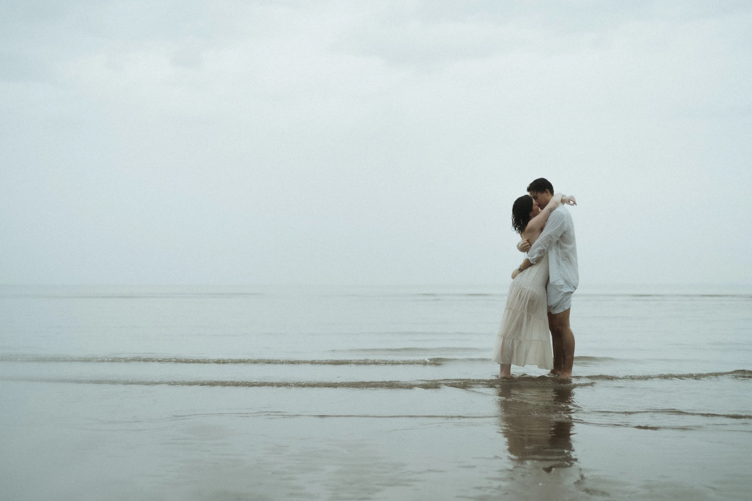 A couple embracing each other in shallow water at the beach on a cloudy day.