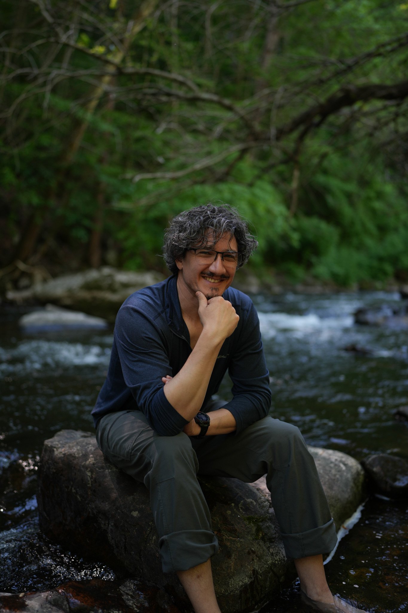 Rick Marren smiling, sitting on a rock in a forest stream