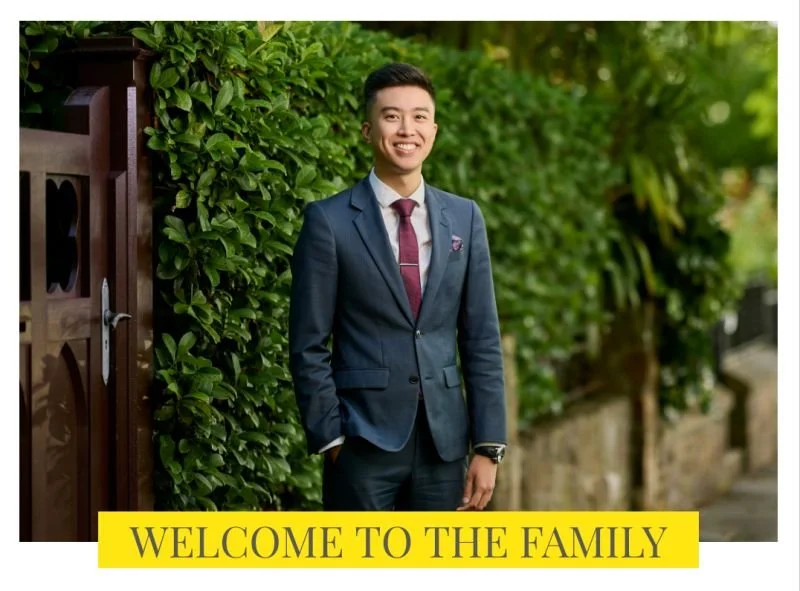 Man in navy suit smiling by greenery, with welcome message banner.