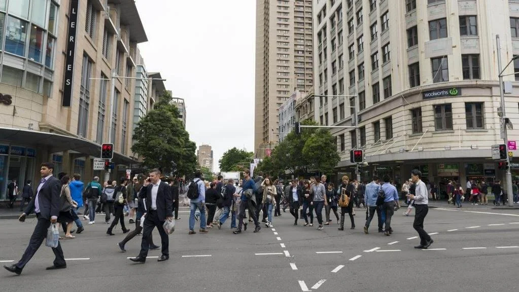 Busy city intersection with people crossing surrounded by tall buildings and traffic lights.