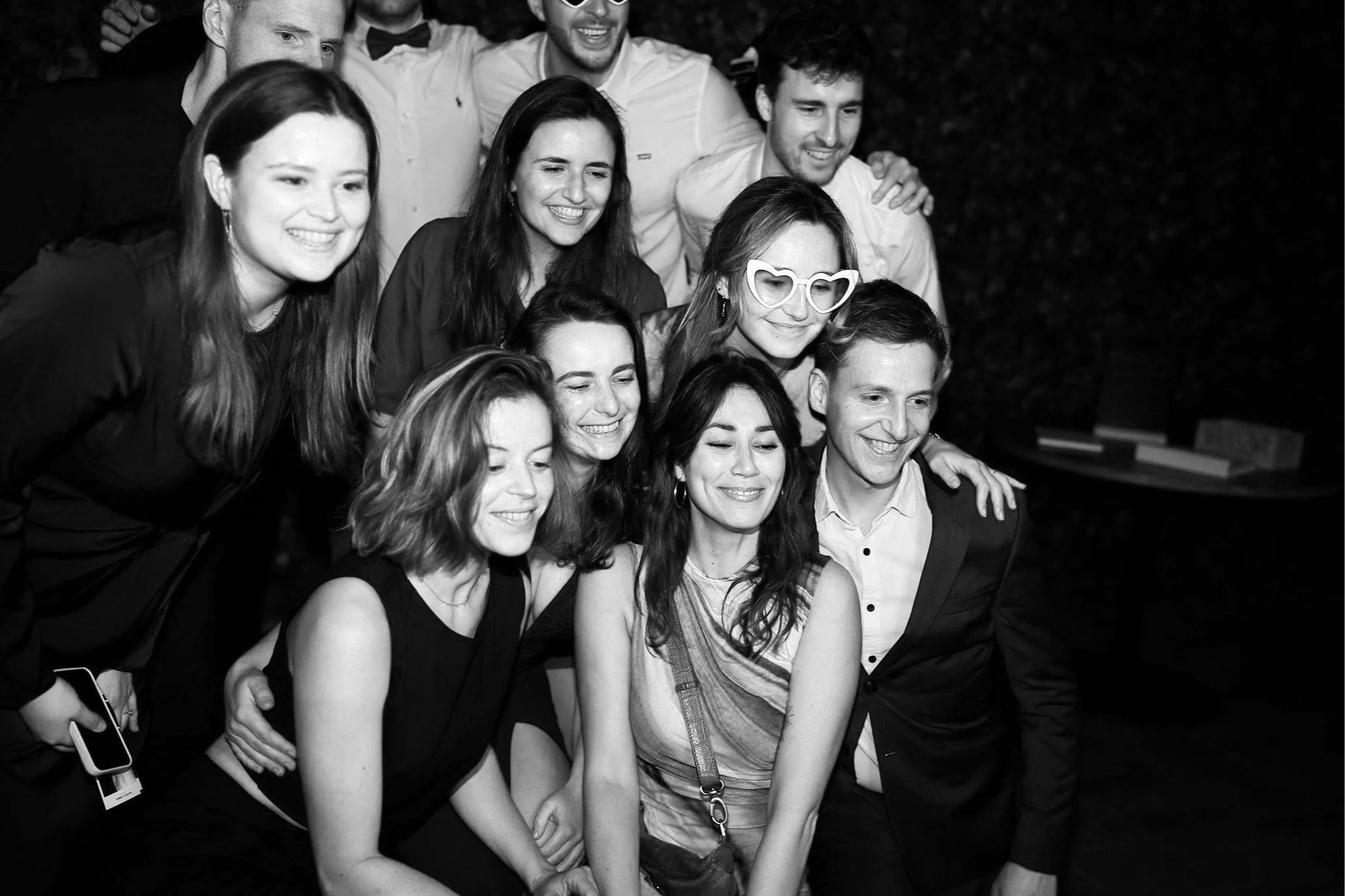 A group of people at a celebration, smiling and posing closely together in a black-and-white photo at night.