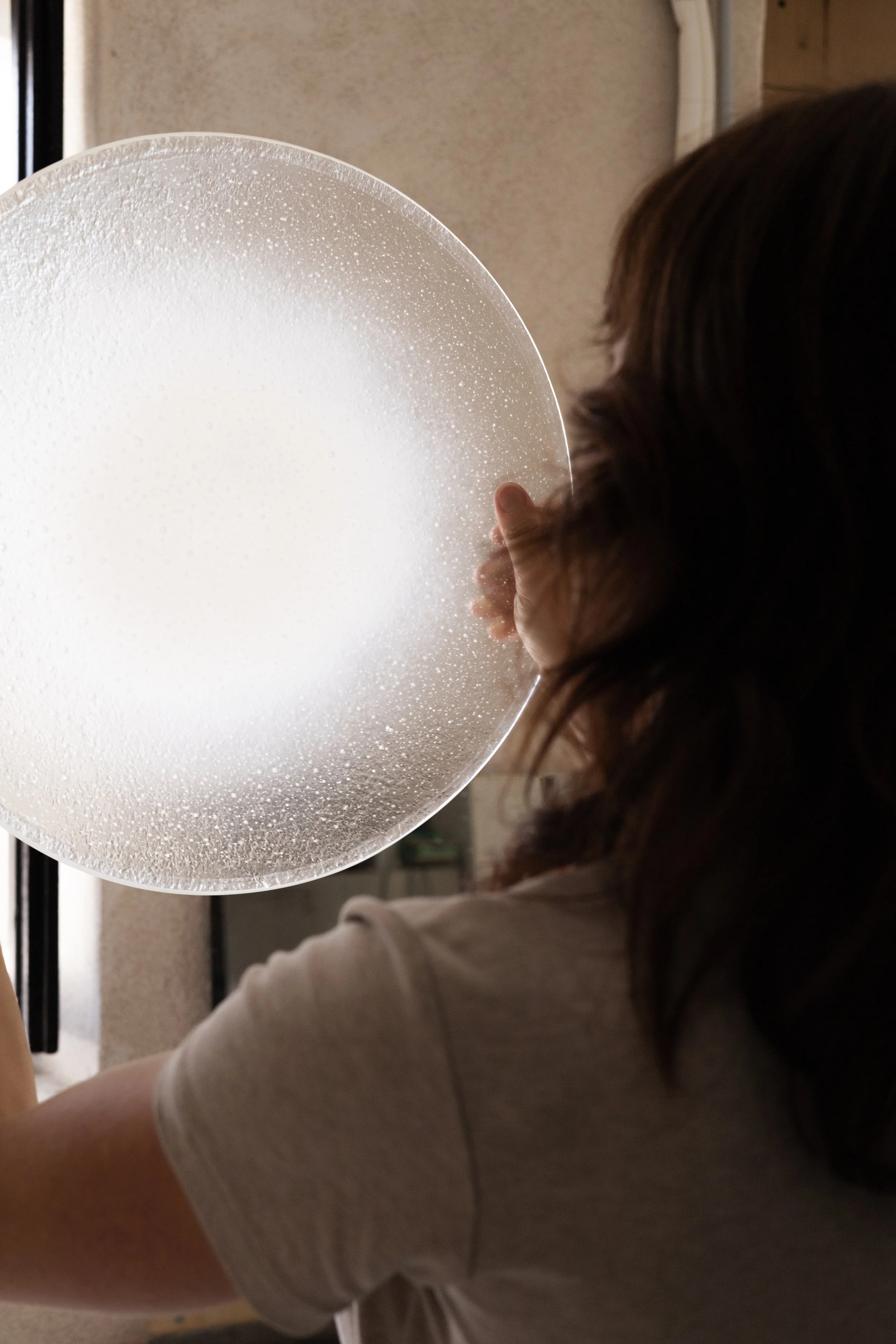 A person with long brown hair and wearing a beige shirt is holding a large white balloon decorated with small white dots.