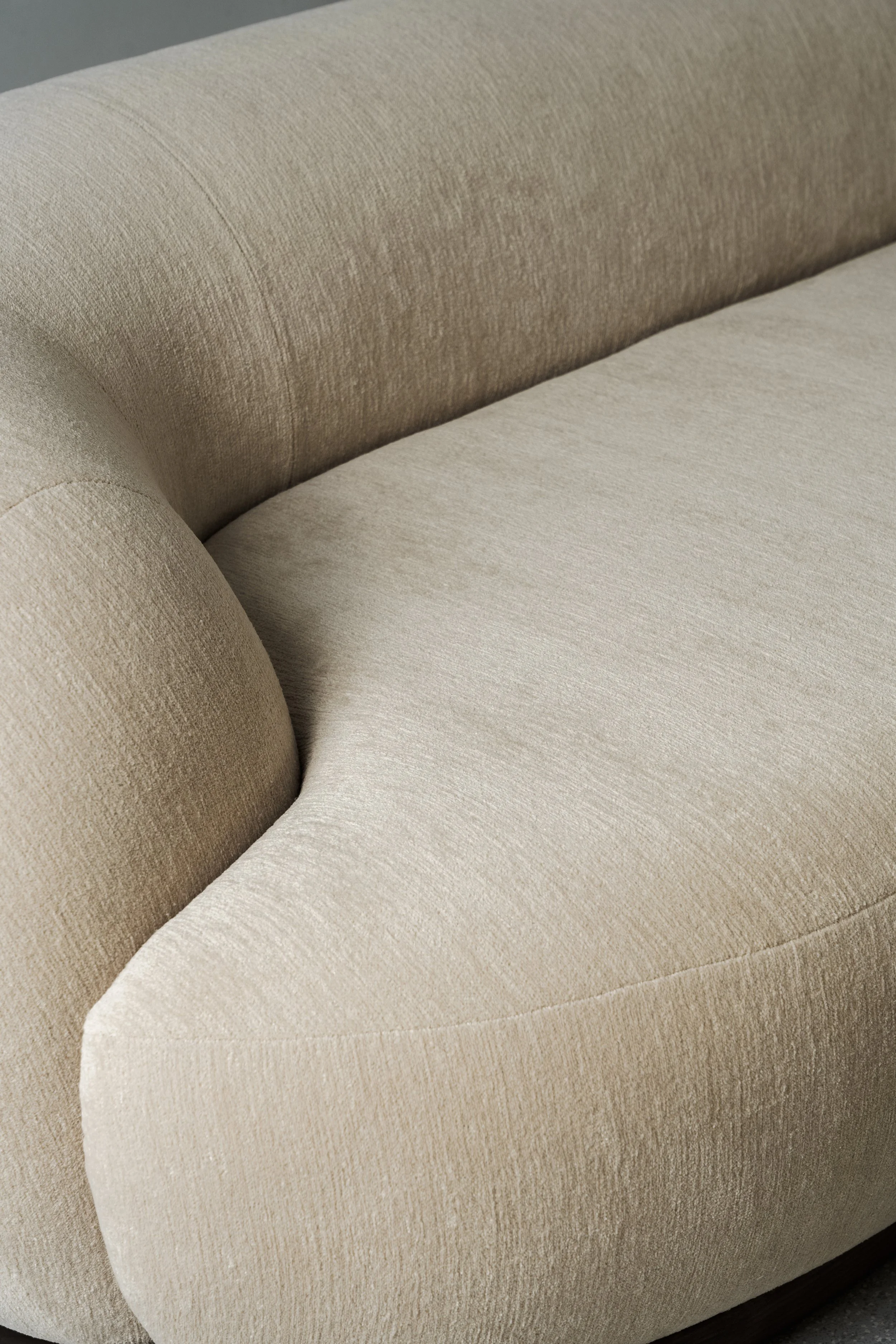 Close-up of a beige upholstered sofa with rounded armrest and textured fabric.