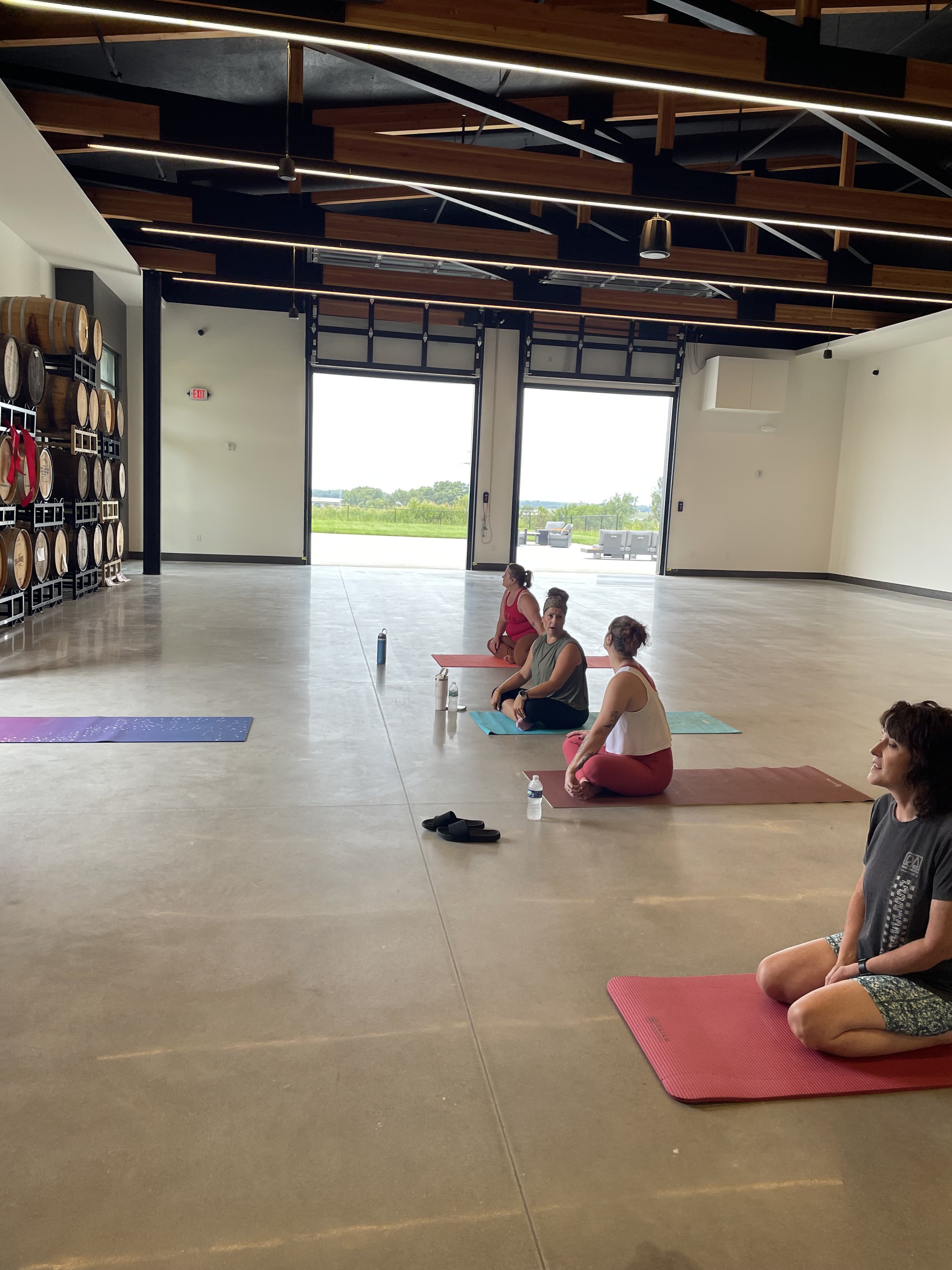 People practicing yoga in a spacious indoor studio with open doors leading outside to a grassy view.