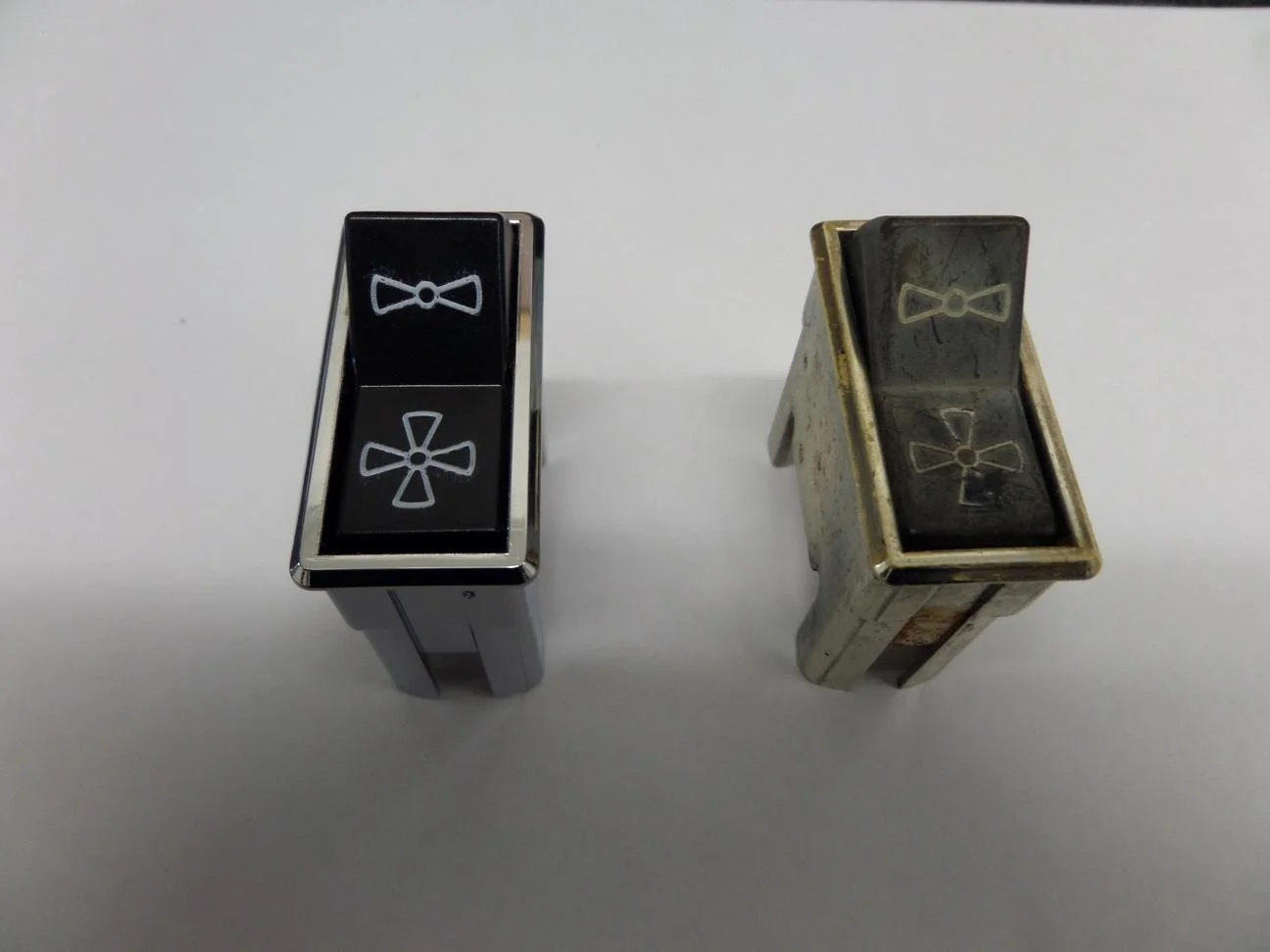 Two vintage mechanical switches with bowtie symbols on the top, one new and shiny, the other old and rusty.