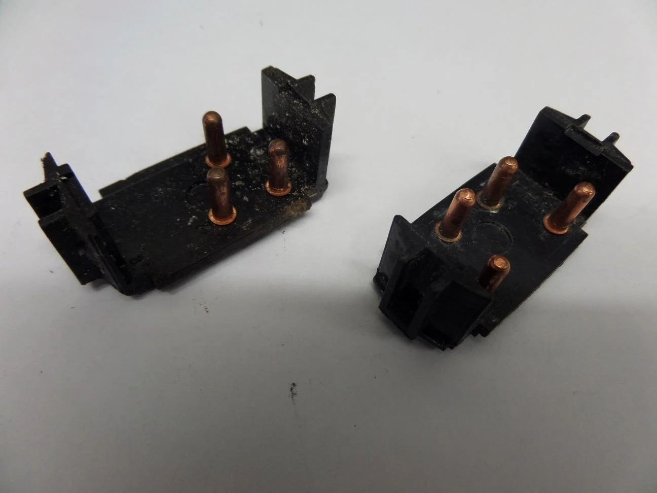 Two black electrical components with copper pins, appearing used or dirty, placed on a white surface.