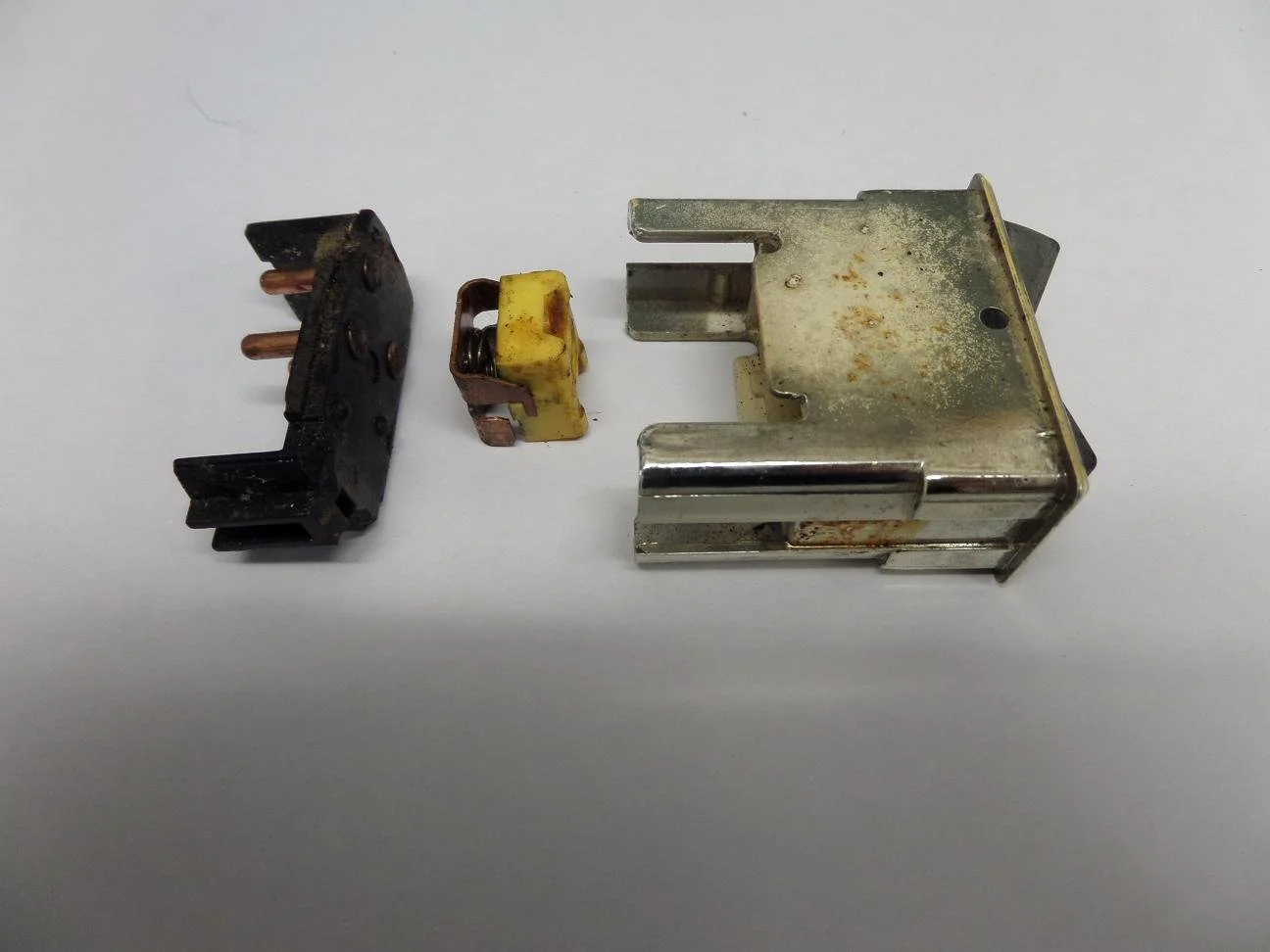 Image showing four disassembled electrical or mechanical components on a white surface, including Black, yellow, and metallic parts.