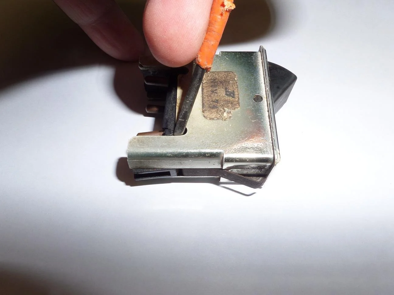 A person holding an old metal switch with a small orange screwdriver, on a white surface.
