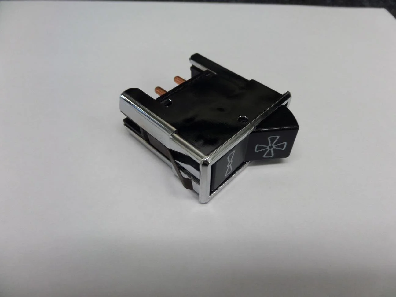 A black and silver toggle switch with fan and light icons, placed on a white surface.