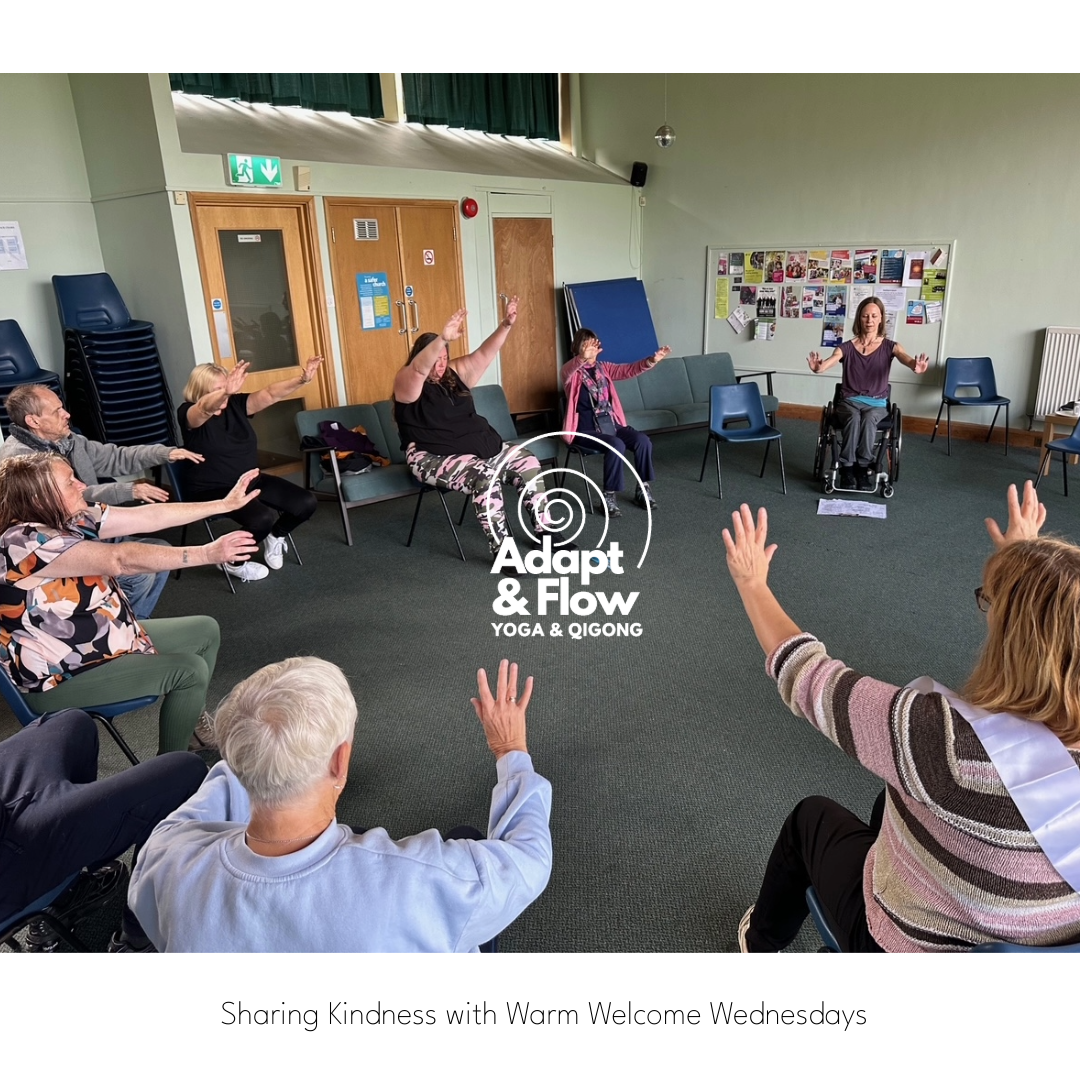 A group of people are practicing seated Qigong with their arms in the air.  A woman in a wheelchair is teaching them