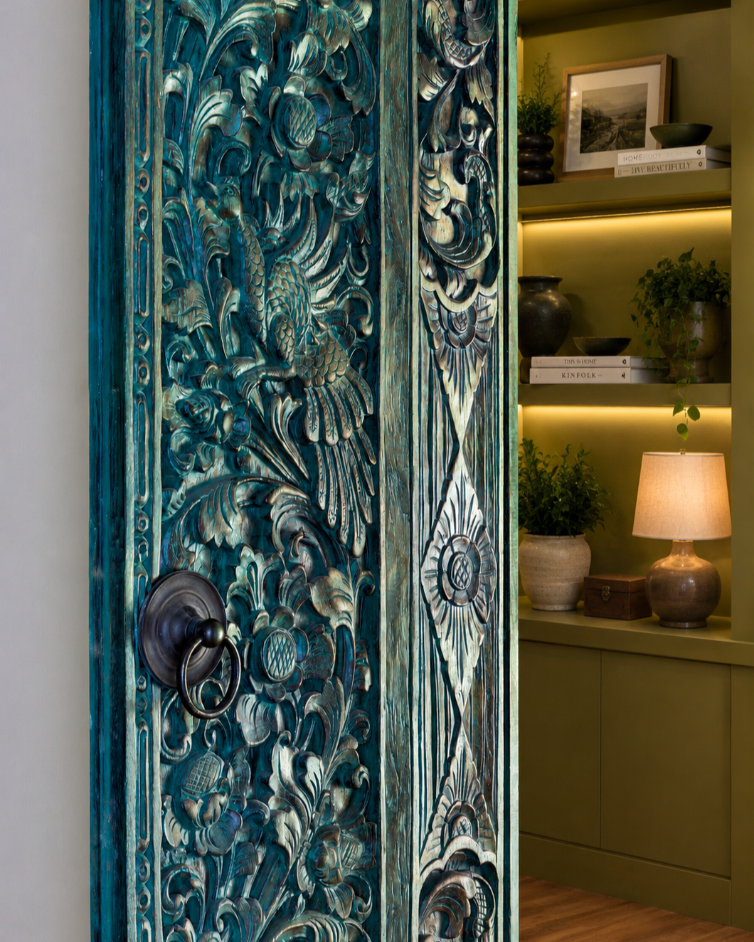 An imported Balinese carved wood door serves as a focal point within this custom library renovation, introducing craftsmanship, texture, and cultural character to the interior architecture.