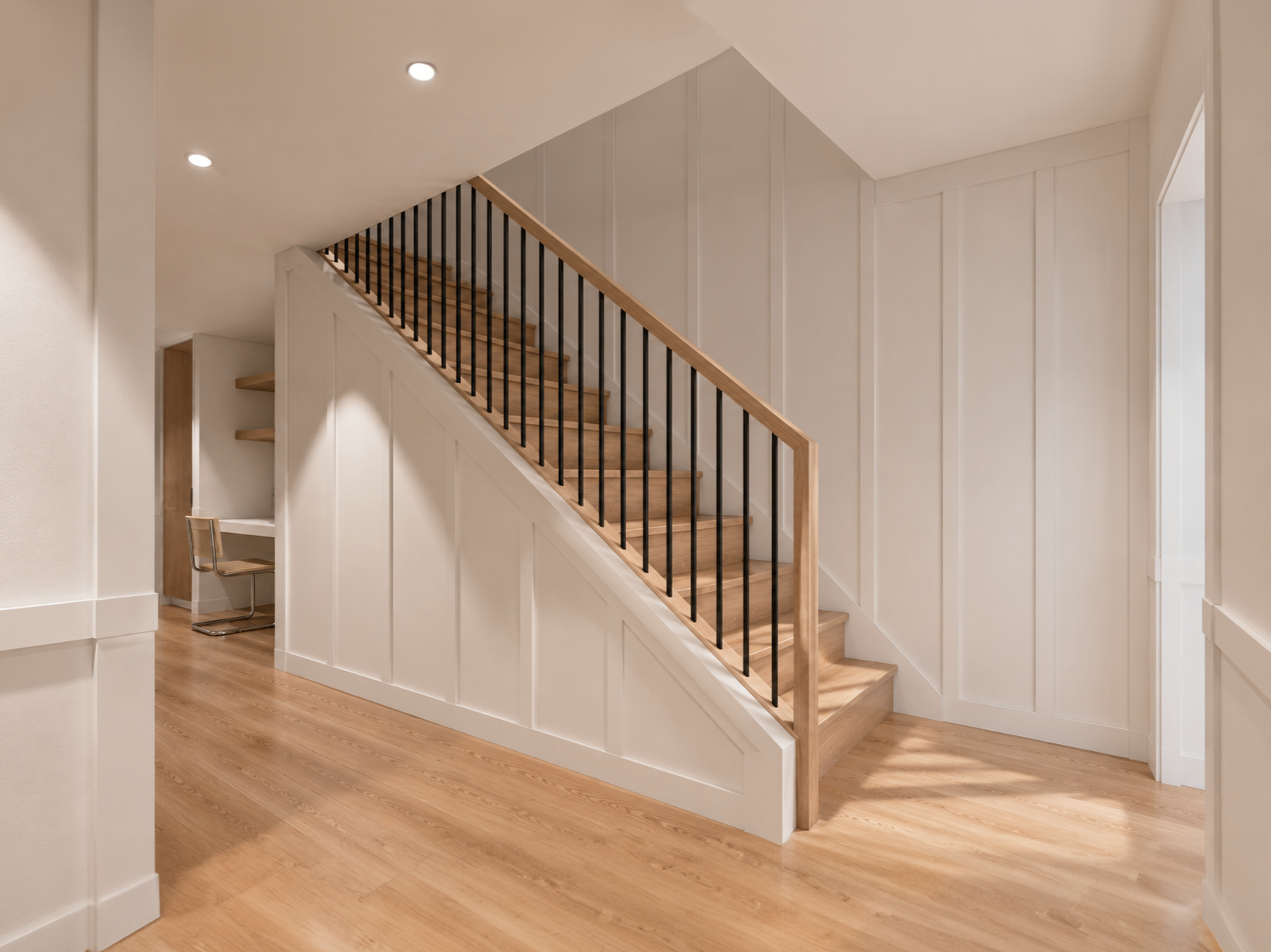 This residential staircase renovation features custom white oak treads, a matching handrail, black metal balusters, and full-height board and batten wall paneling. Designed by From David Designs, the staircase serves as a central architectural featur