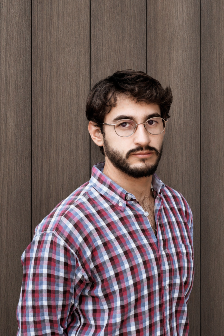 Man wearing glasses and a plaid shirt standing against a wooden background.