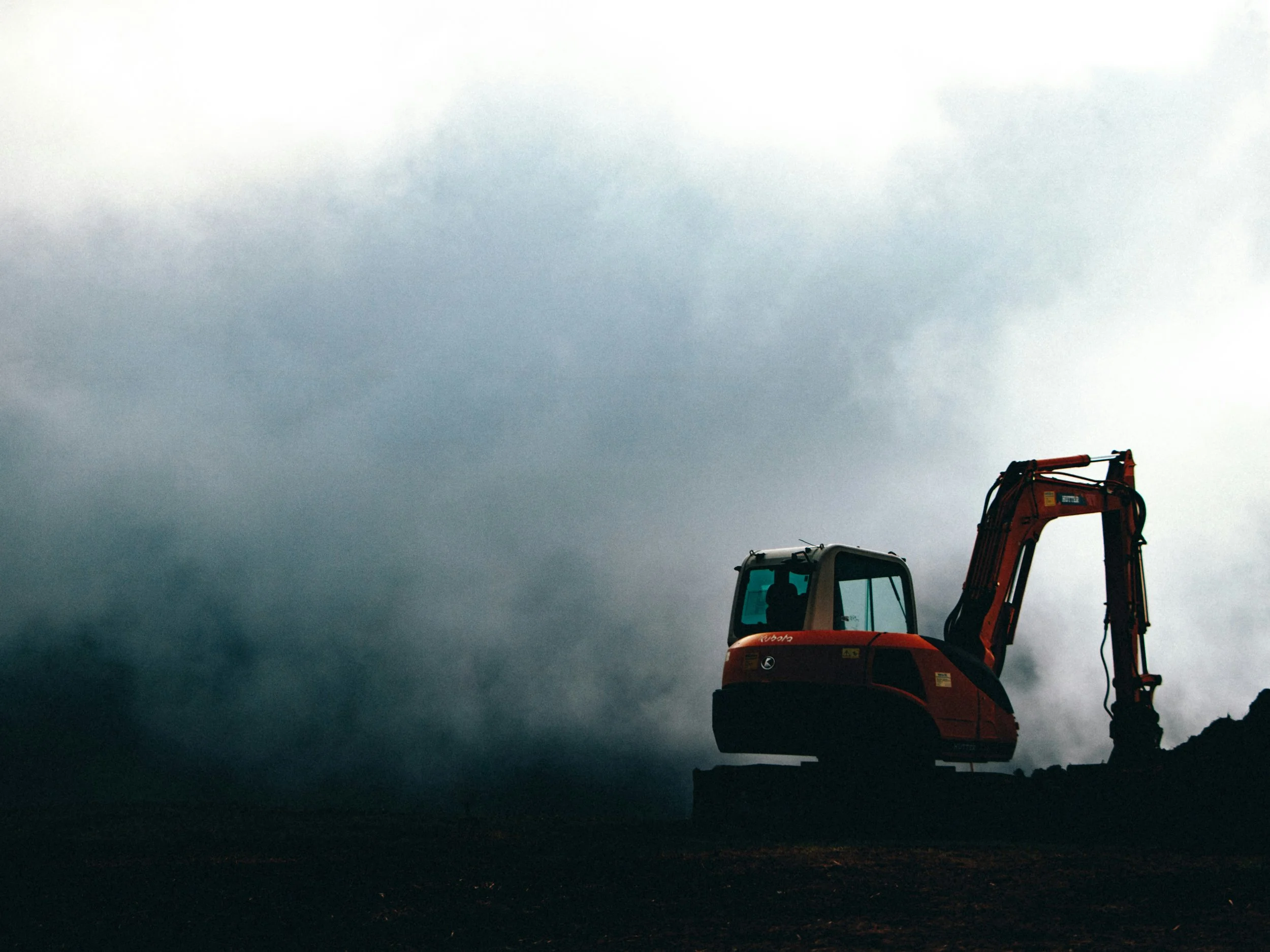 Une pelleteuse rouge sur un terrain sombre avec un ciel nuageux.