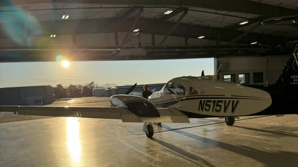 Small training airplane parked inside an airport hangar with the sun setting outside.