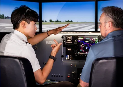 A young female pilot instructor and an older male student in an airplane cockpit, reviewing flight simulation screens.