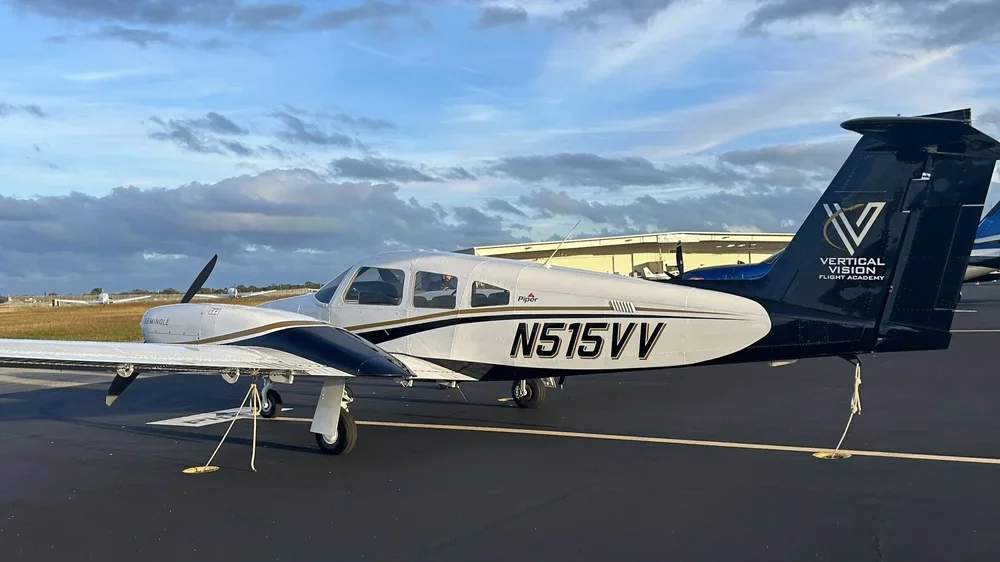 Small training airplane parked on runway with cloudy sky in the background.